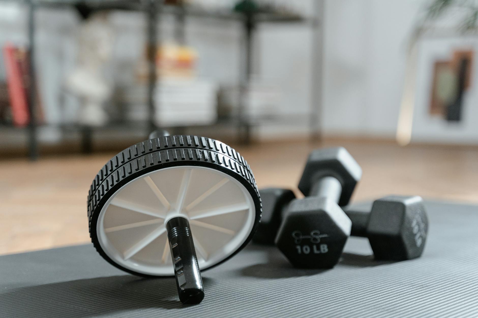 Ab roller and dumbbells on yoga mat, perfect for a home workout routine and healthy lifestyle. - at home strength