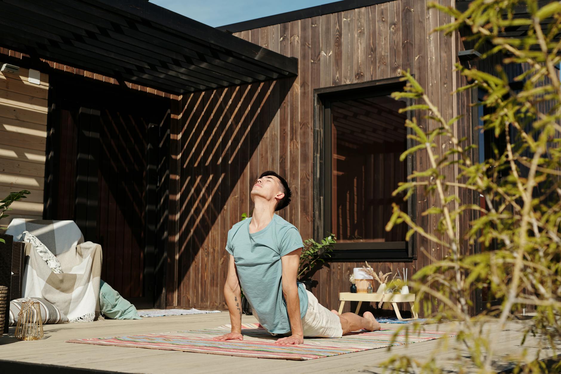 Adult man engaging in yoga stretch on a sunny outdoor veranda, showcasing a healthy lifestyle. - home wellness retreat