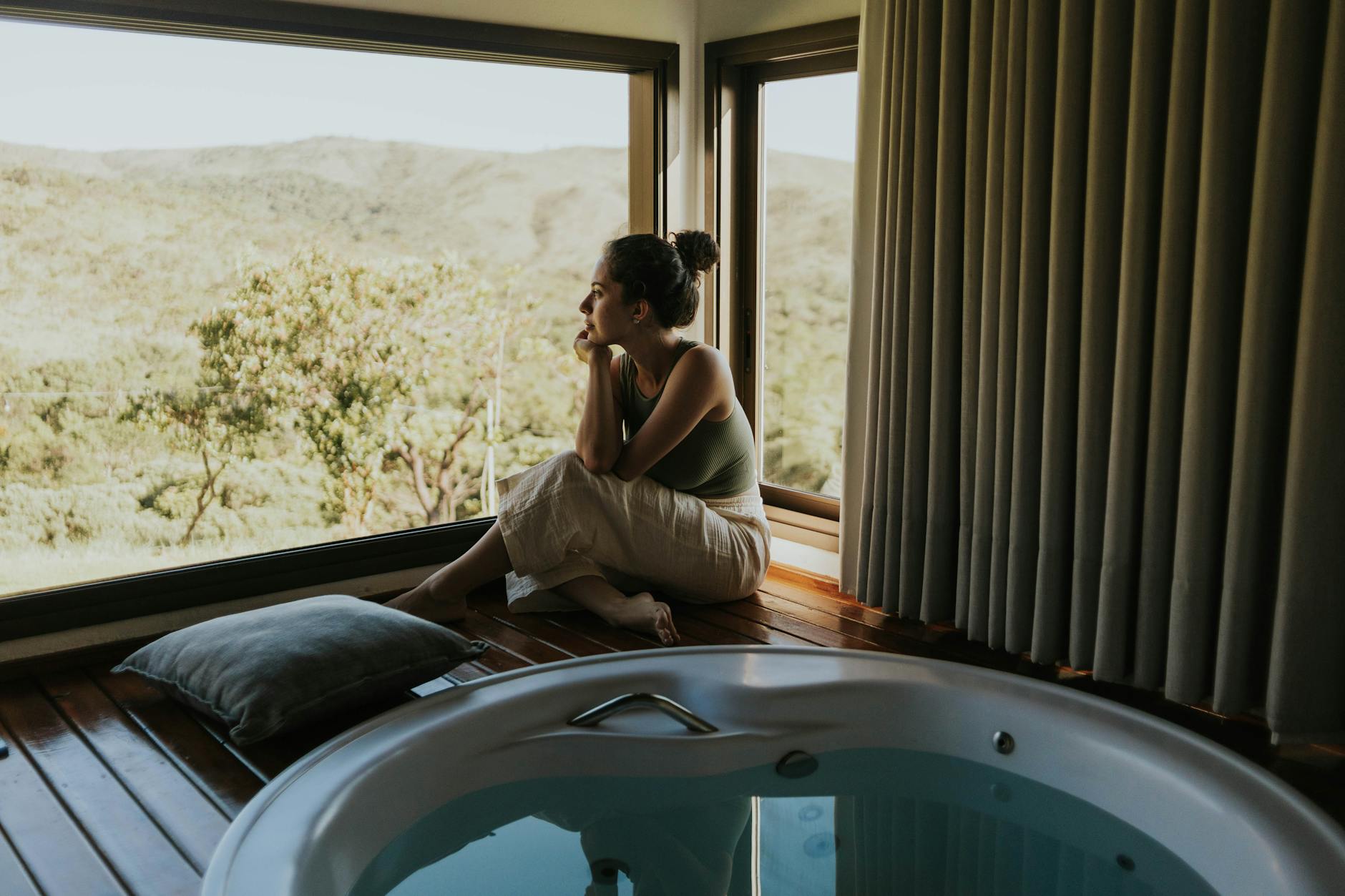Woman gazing through window beside indoor jacuzzi overlooking mountains. - home wellness retreat