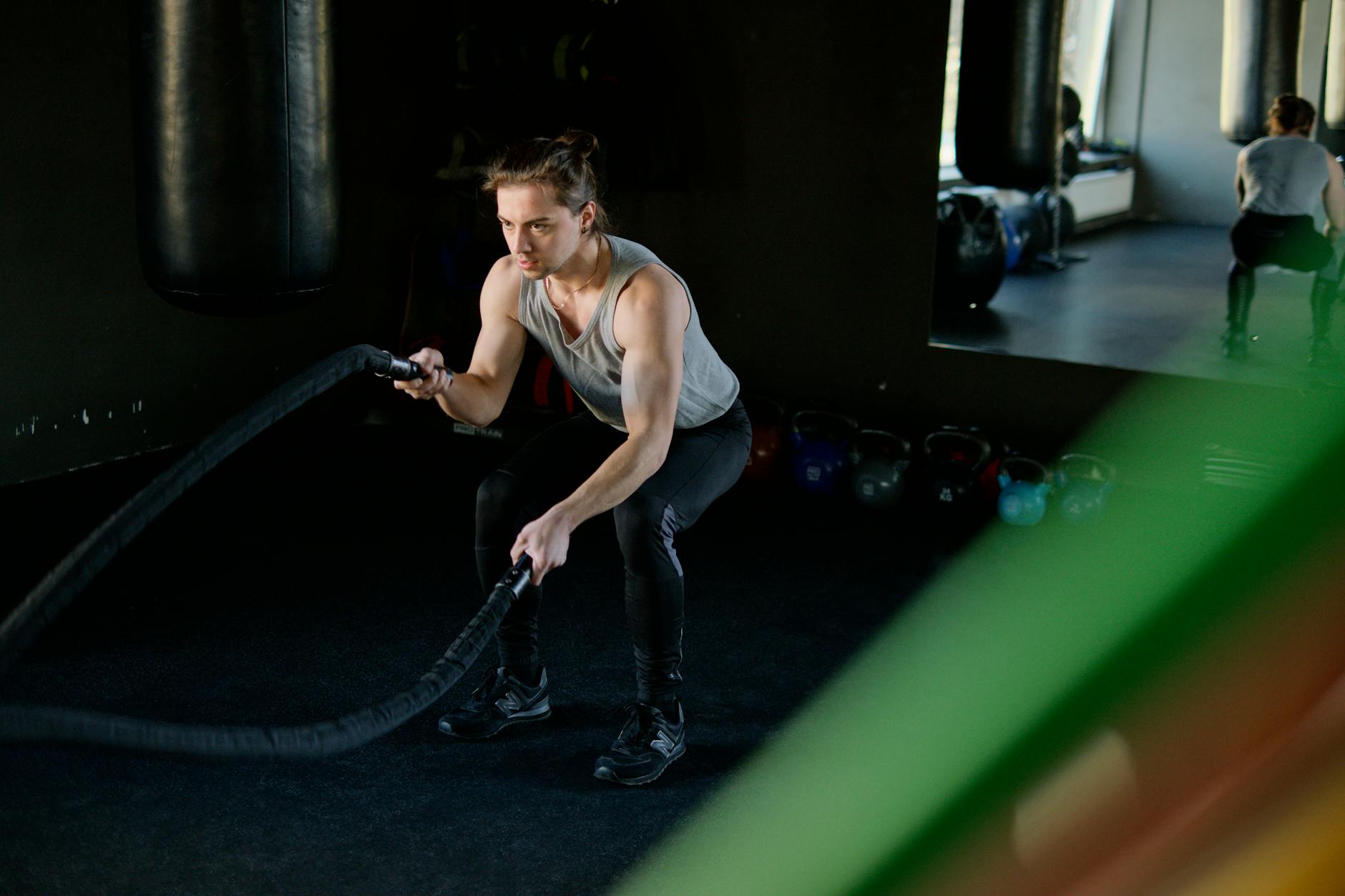 Man engages in an intense battle rope workout in a gym, focusing on fitness and strength. - interval training cardio