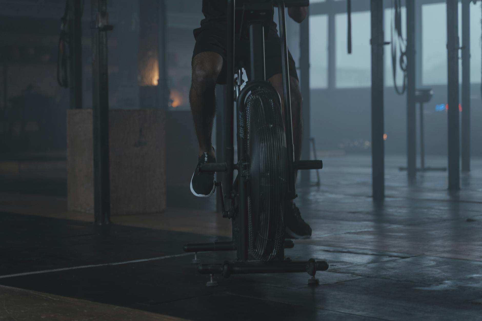 Close-up of a person exercising on a stationary bike in a dimly lit gym setting. - interval training fitness