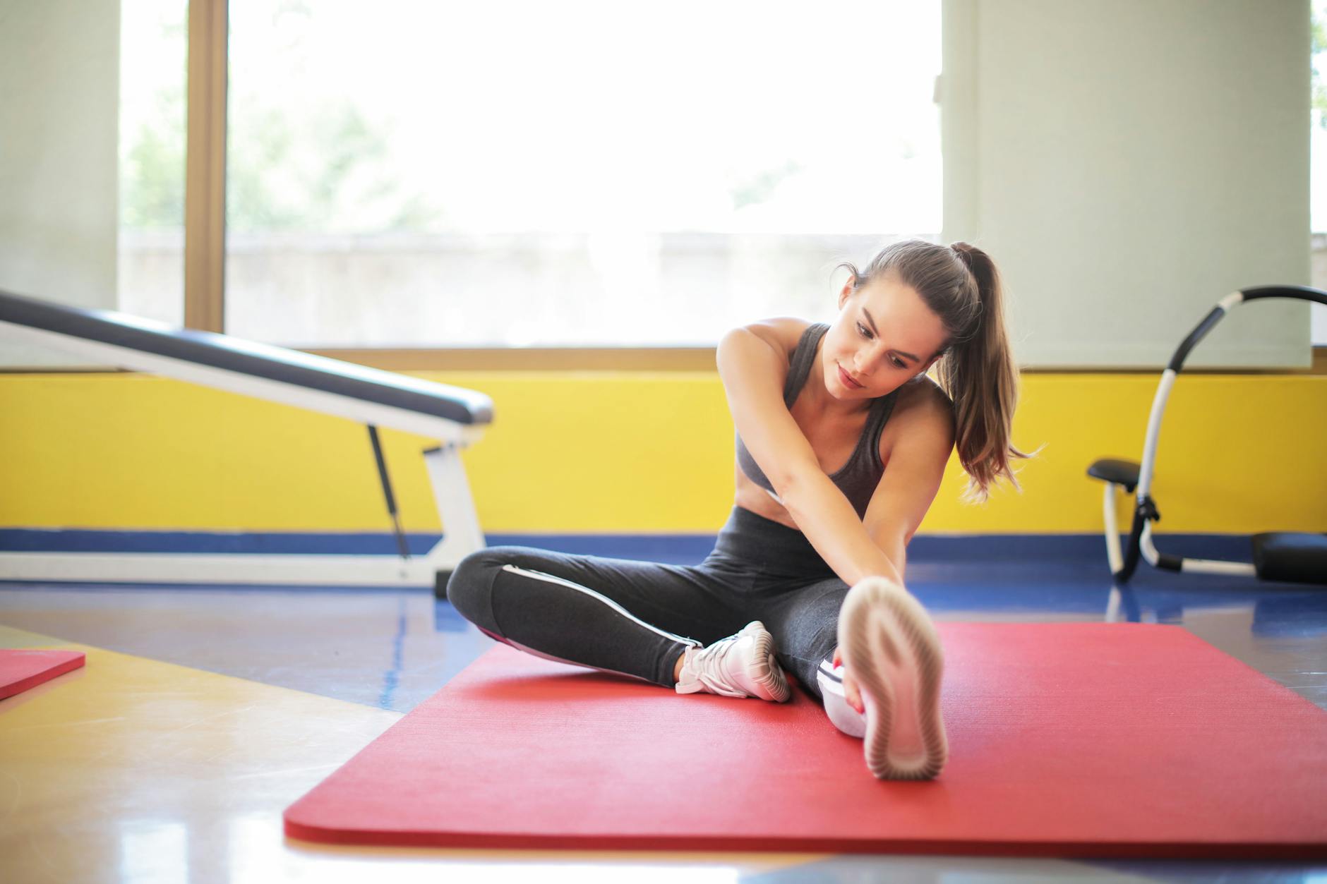 Female athlete stretching on a red yoga mat indoors, emphasizing flexibility and fitness. - knee flexibility exercises