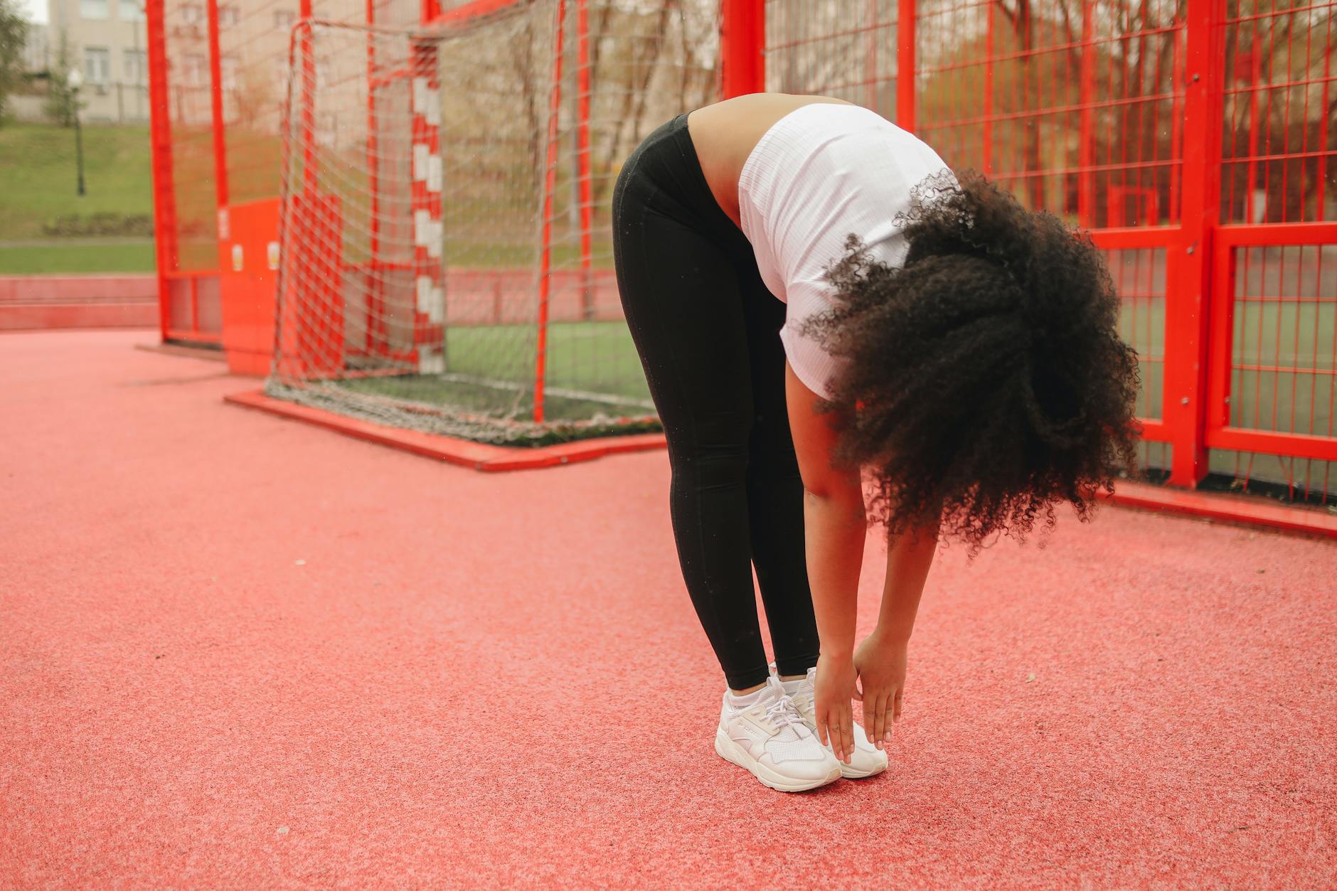 Woman exercising by stretching in a vibrant red outdoor sports court, emphasizing fitness and wellness. - leg flexibility exercises