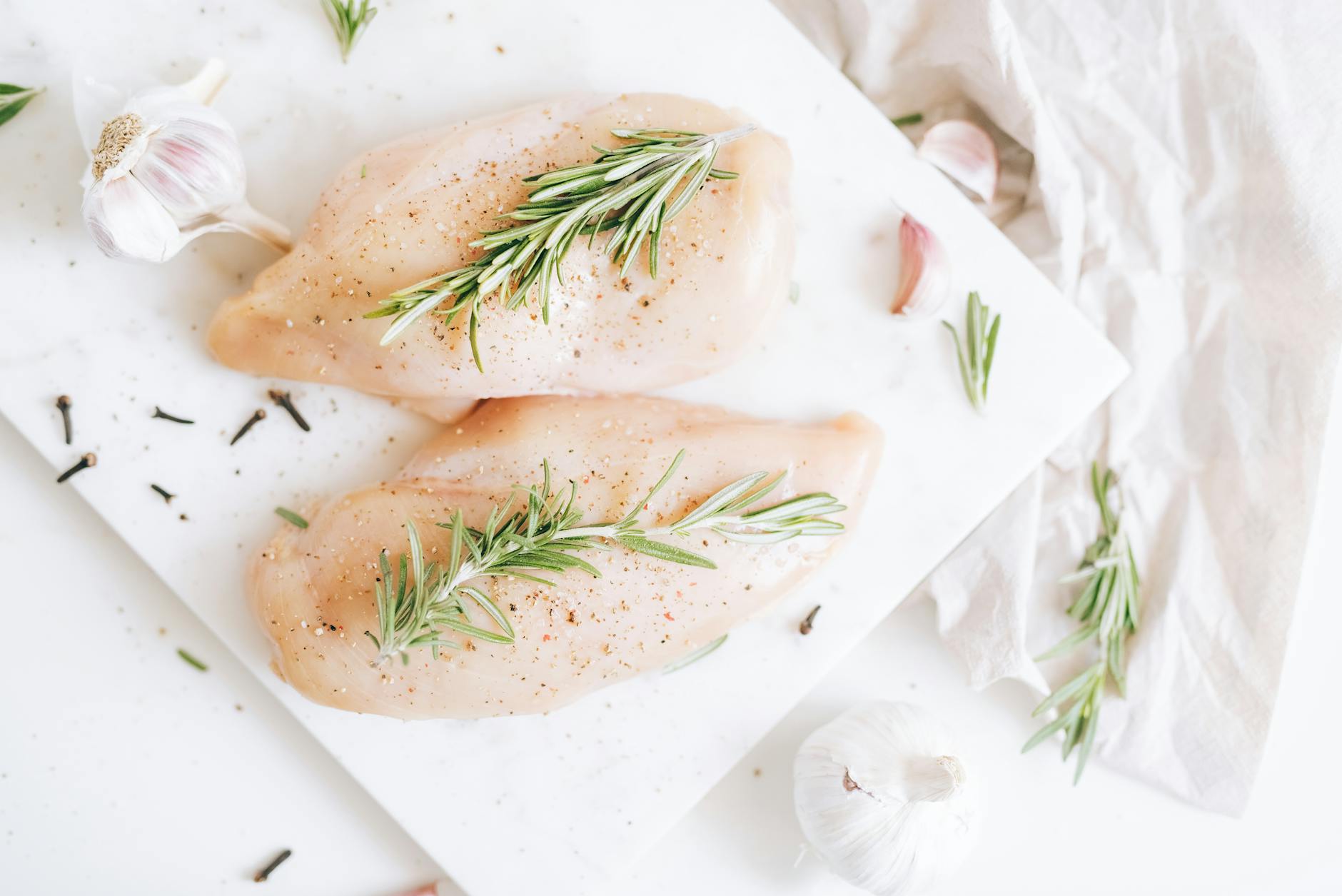Raw chicken breasts seasoned with rosemary and garlic on a cutting board. - low carb chicken