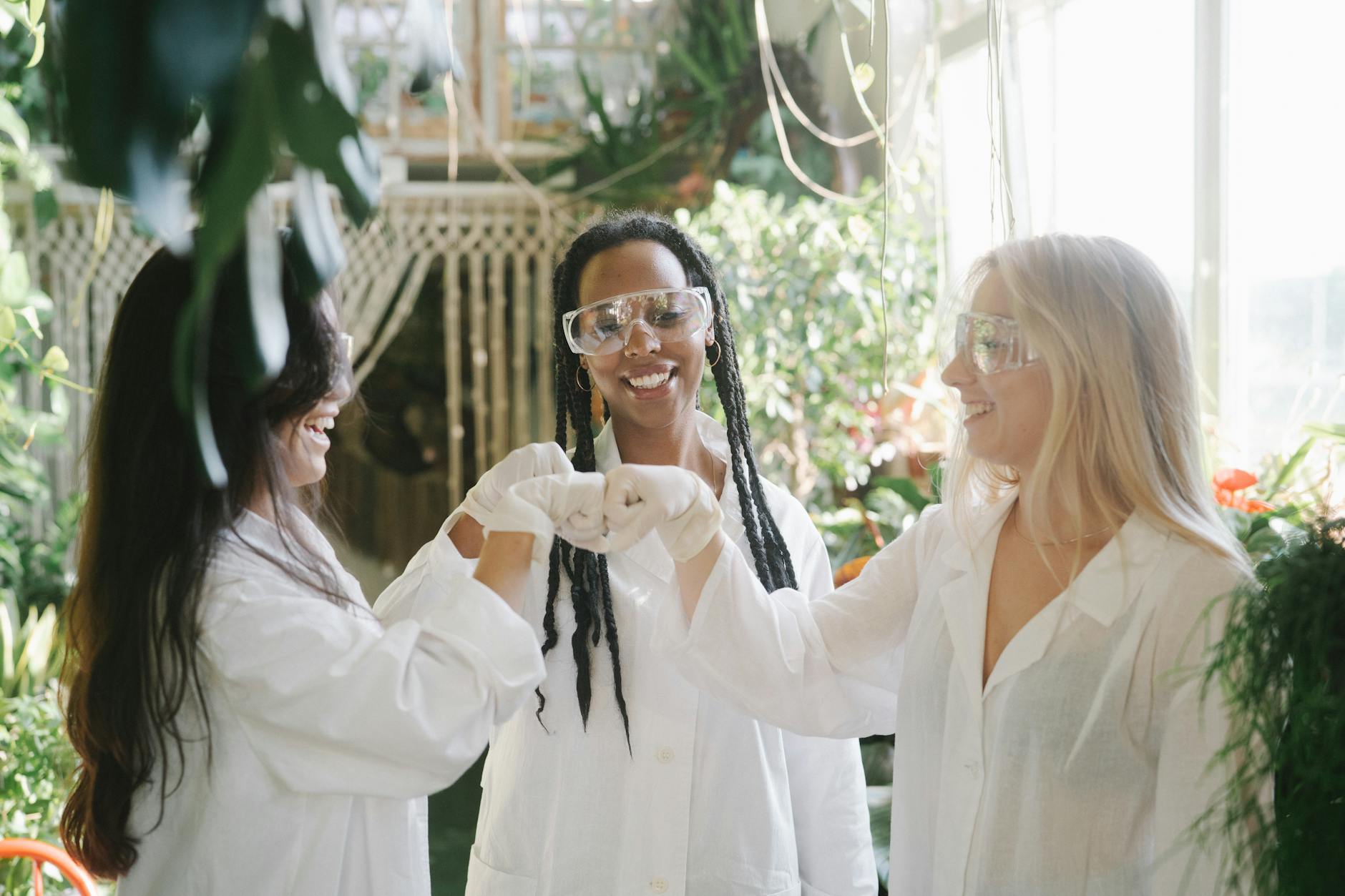 Three women scientists wearing safety glasses and lab gowns working together in a greenhouse. - magnesium for women