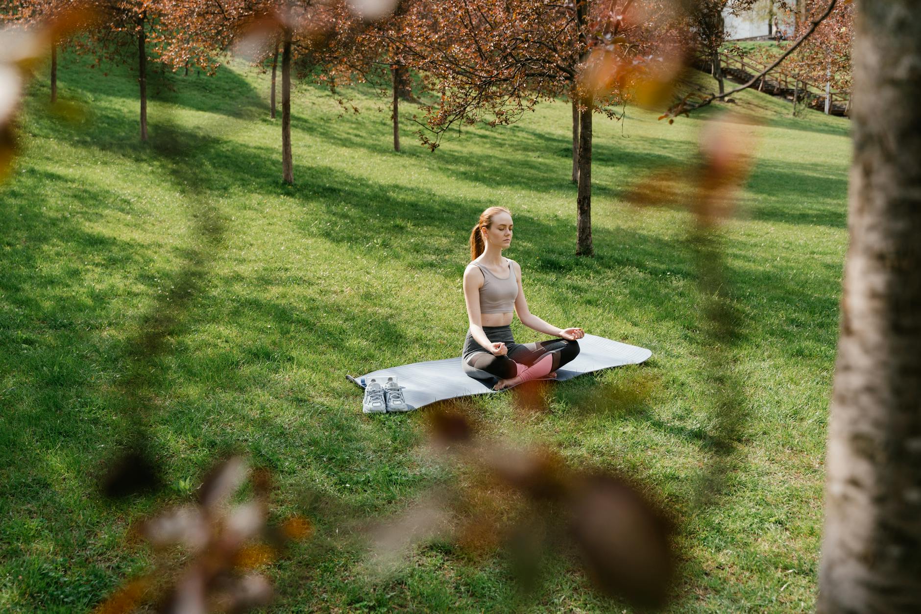 A woman meditating on a yoga mat in a sunny park surrounded by trees. - mental clarity spring