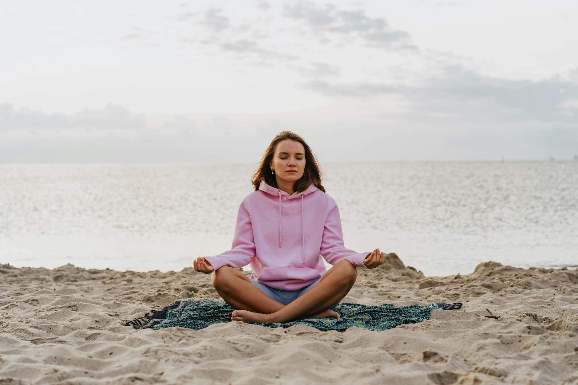 Woman meditating on a beach at sunrise, embodying peace and relaxation in nature. Ideal for wellness themes. - mental clarity tips