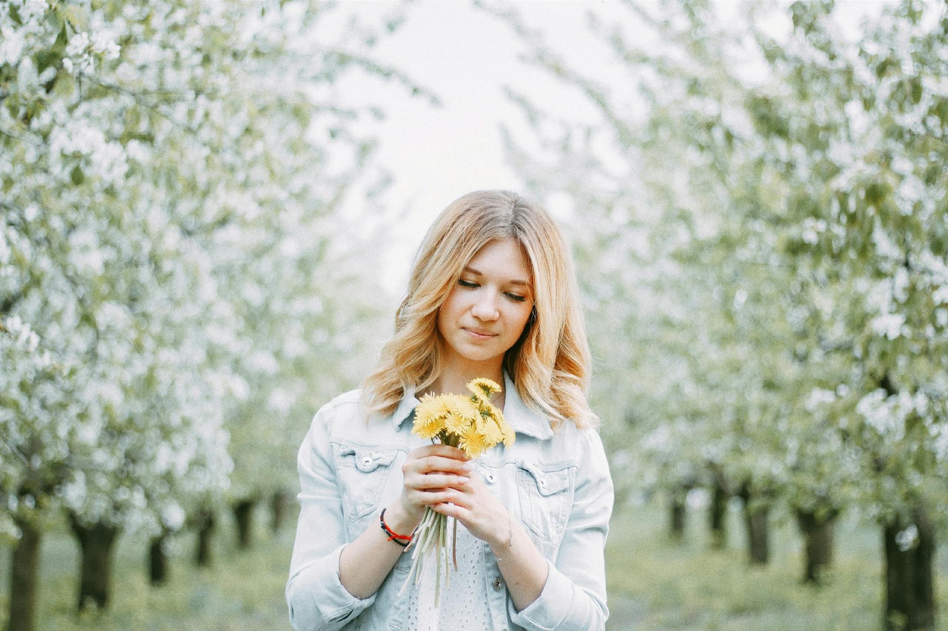 A young woman with blond hair holds dandelions in a blooming orchard, signifying springtime beauty. - metabolism reset spring