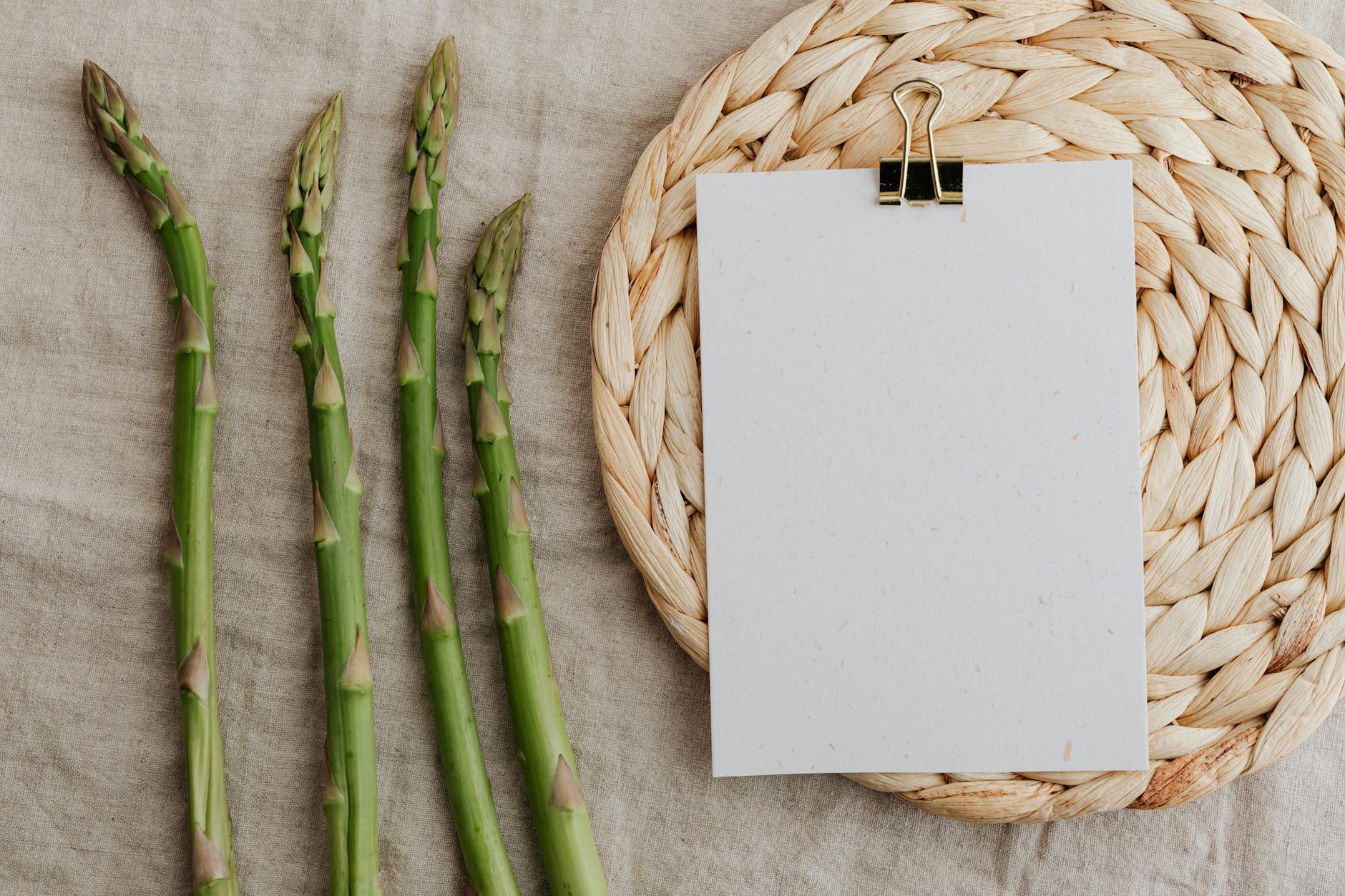 Fresh asparagus arranged on rustic fabric with a blank paper on a woven mat, perfect for culinary themes. - mindful spring eating