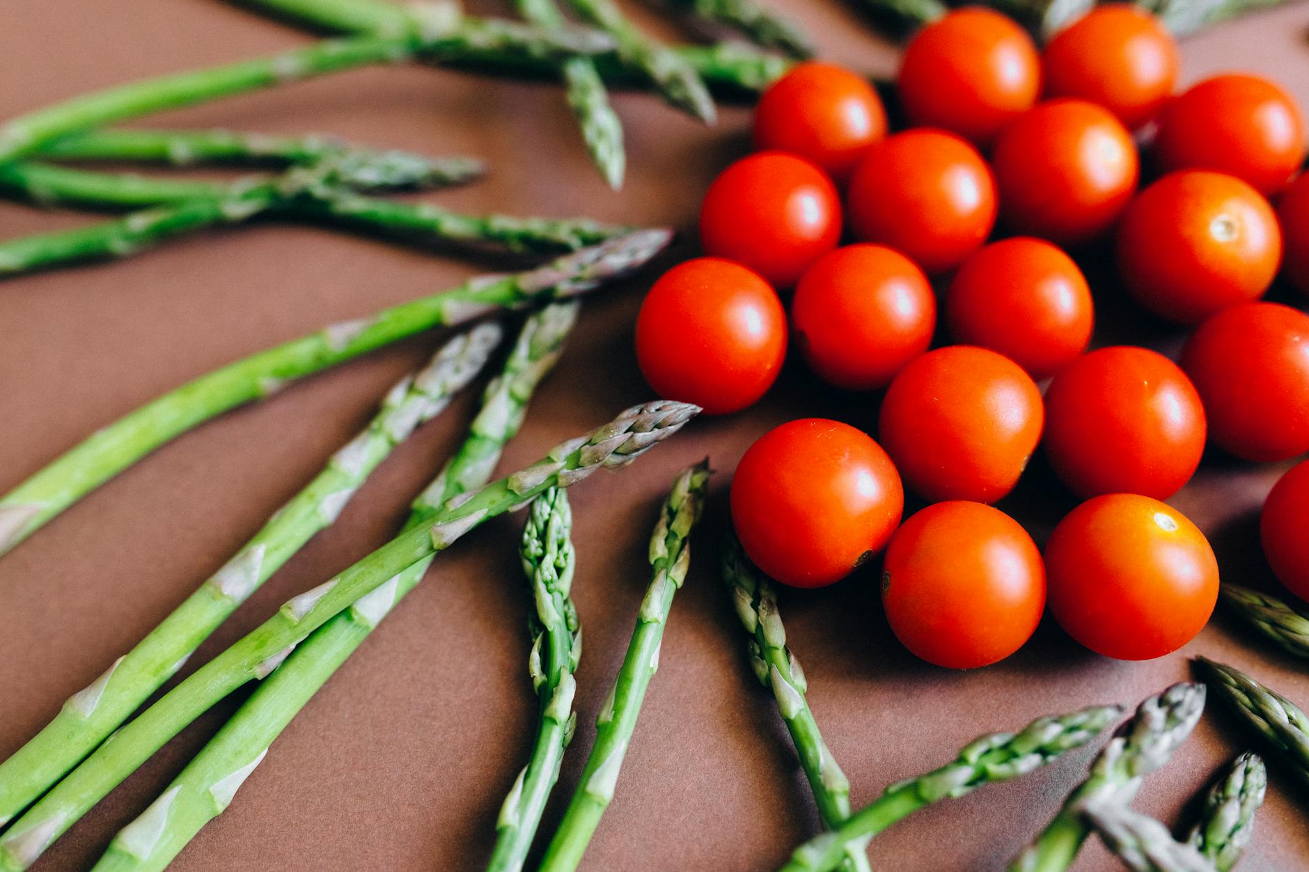 Close-up of fresh asparagus and cherry tomatoes arranged on a brown background. - mindful spring eating