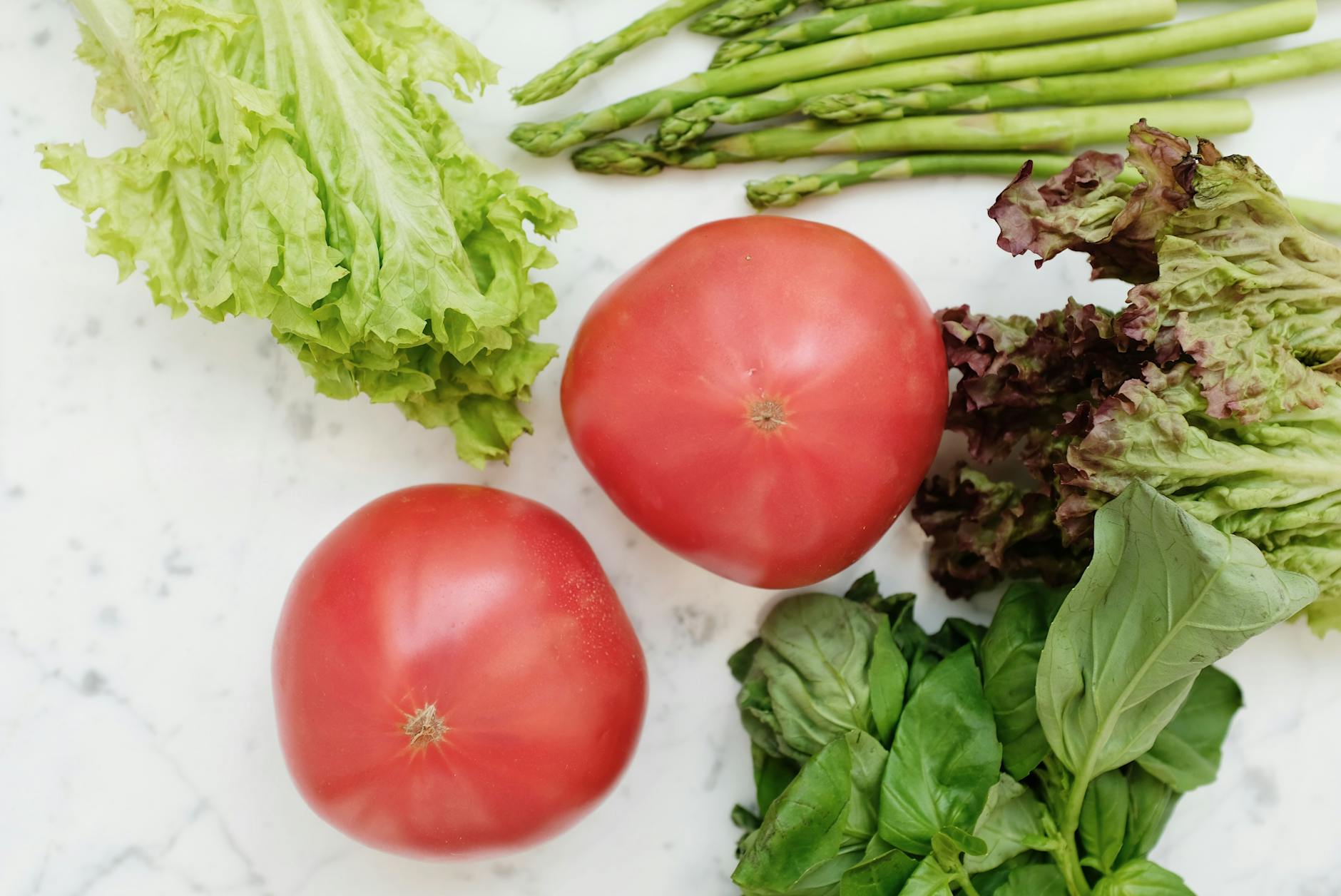 Top view of fresh vegetables including lettuce, asparagus, tomatoes, and basil on marble surface. - mindful spring eating
