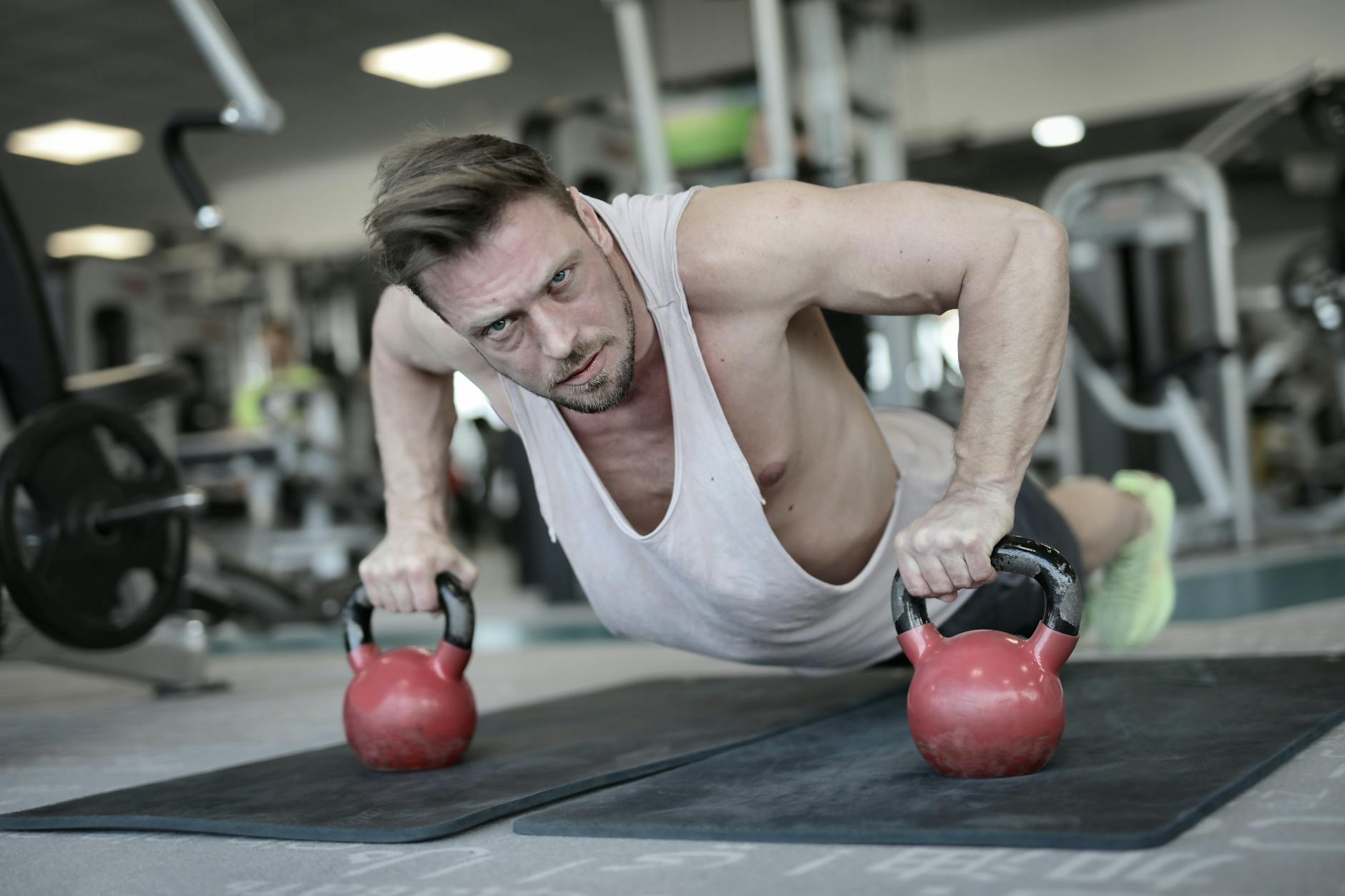 Low angle of powerful male bodybuilder in sportswear pushing up on kettlebells during training and looking at camera - muscular endurance exercises