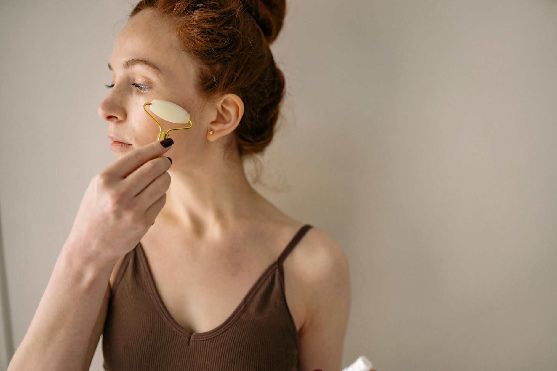A woman applying a jade face roller as part of her skincare routine, promoting self-care. - natural anti aging skin