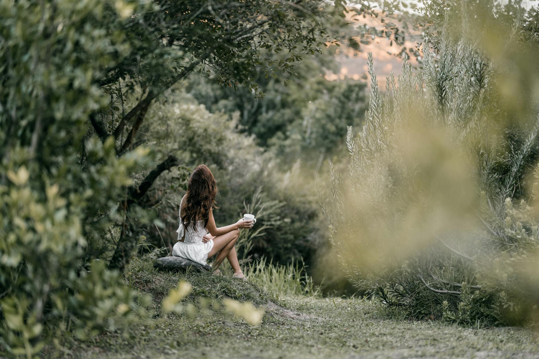 Woman in a white dress enjoying coffee in a lush green forest setting. - nature digital detox