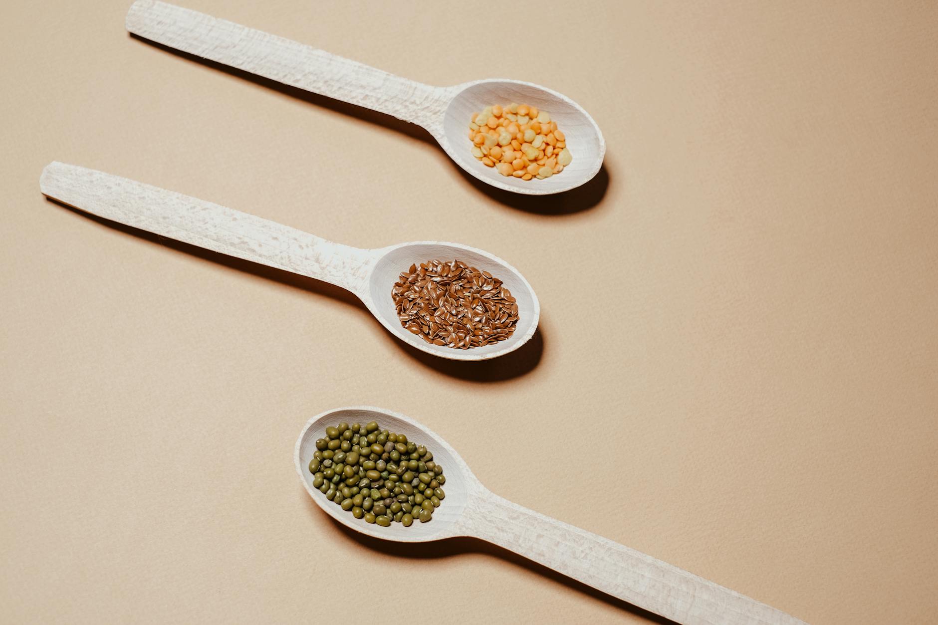 Flat lay of mung beans, flaxseeds, and split peas in wooden spoons, showcasing natural grains. - organic plant protein