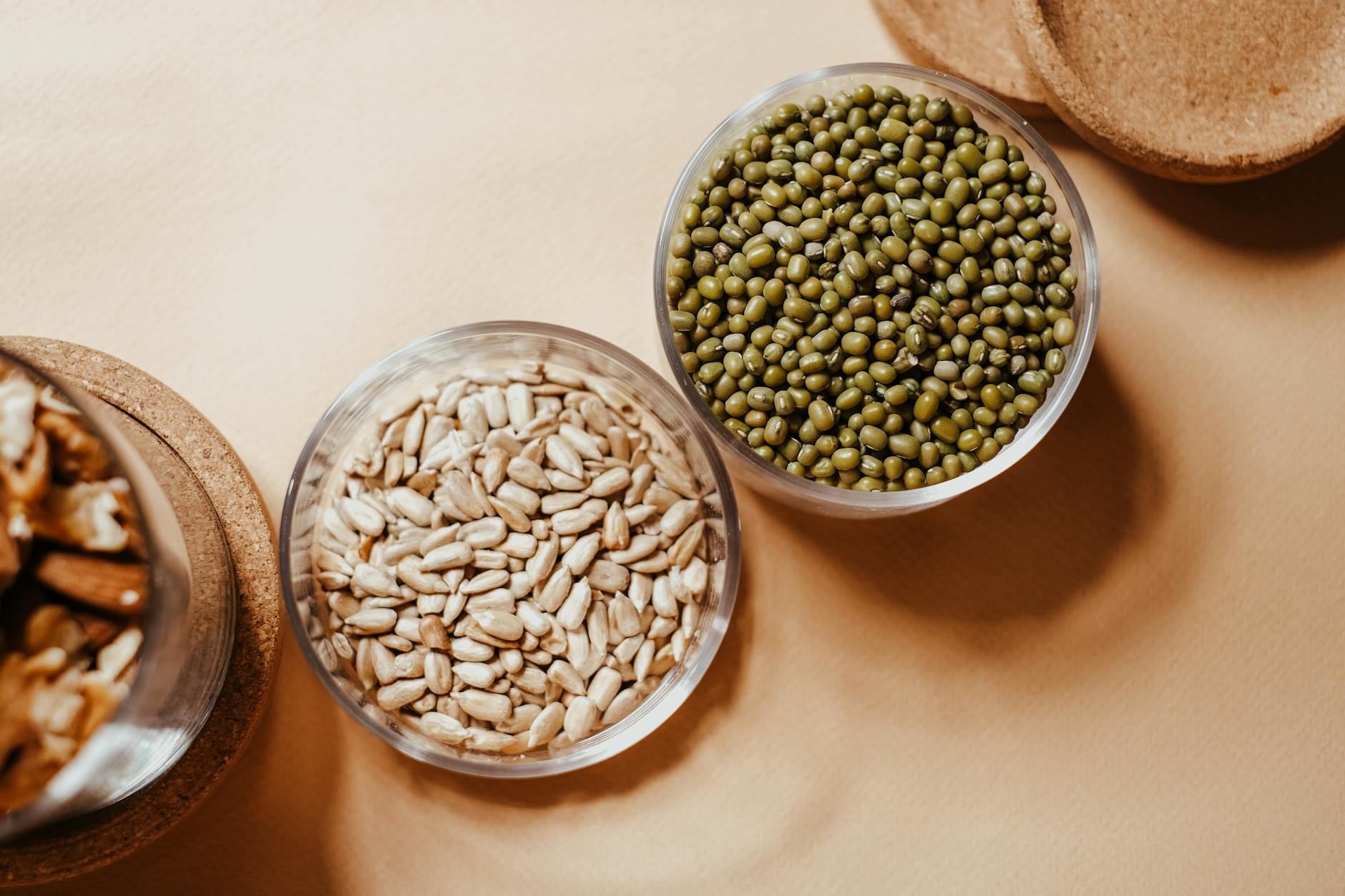 Glass bowls filled with organic mung beans and sunflower seeds on a neutral background. - organic plant protein