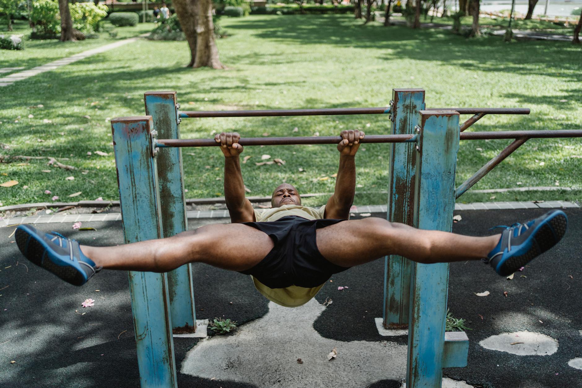 A man performing a challenging workout on parallel bars in an outdoor park setting. - outdoor bodyweight workout