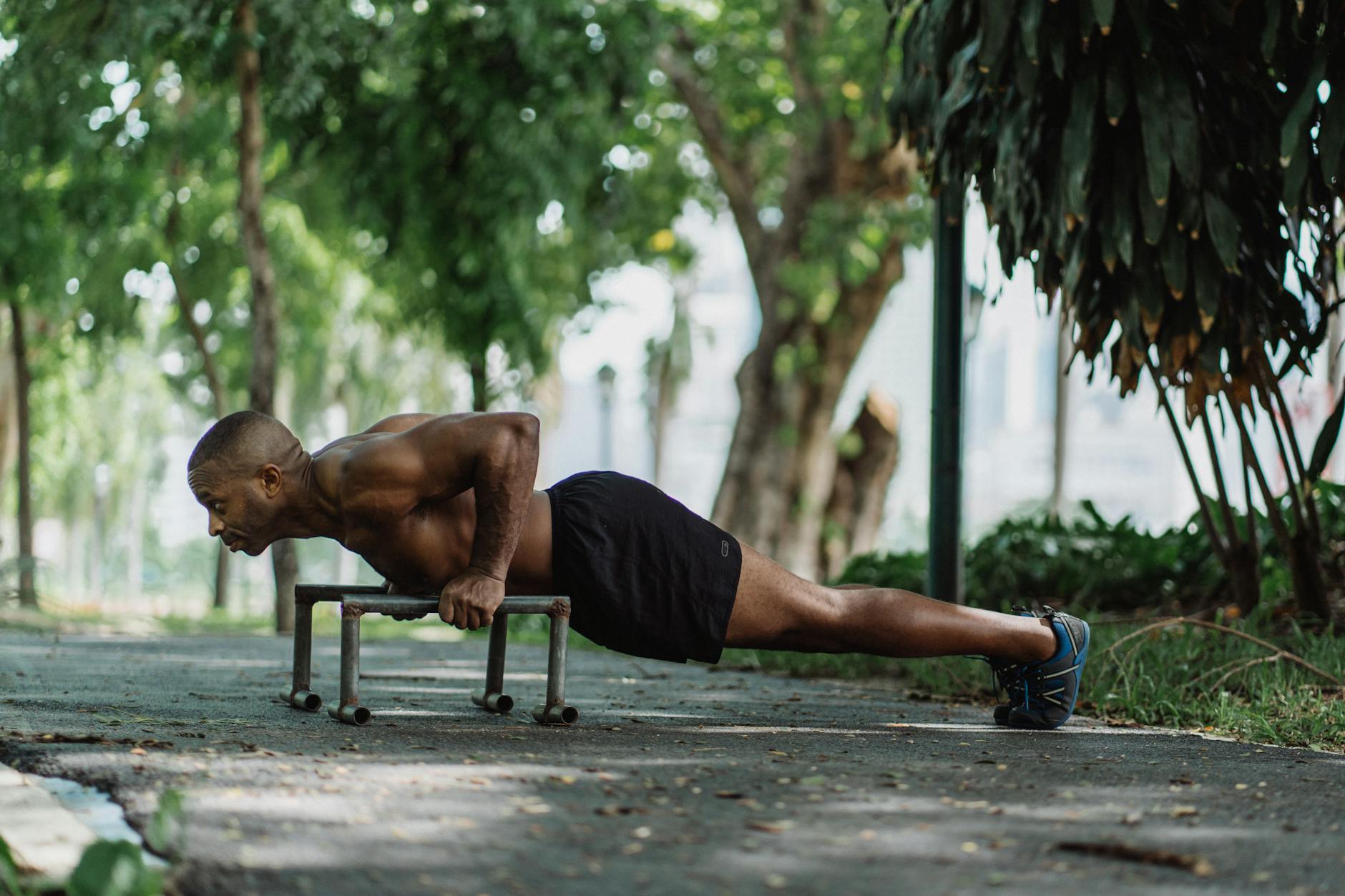 Man doing push-ups on bars in a park, showcasing strength and fitness outdoors. - outdoor bodyweight workout