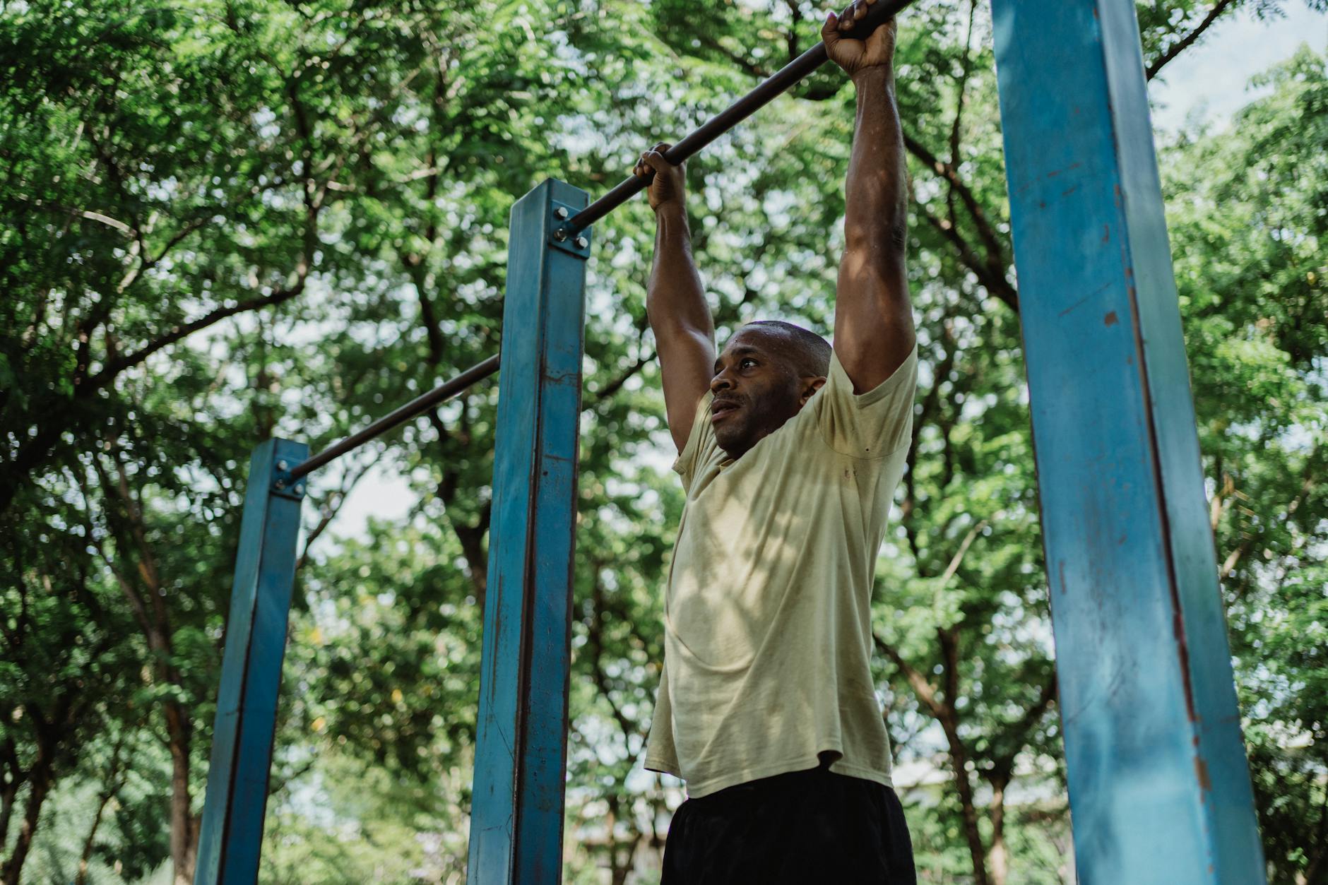 A man doing pull-ups on blue bars in a park, showcasing fitness and strength. - outdoor bodyweight workout