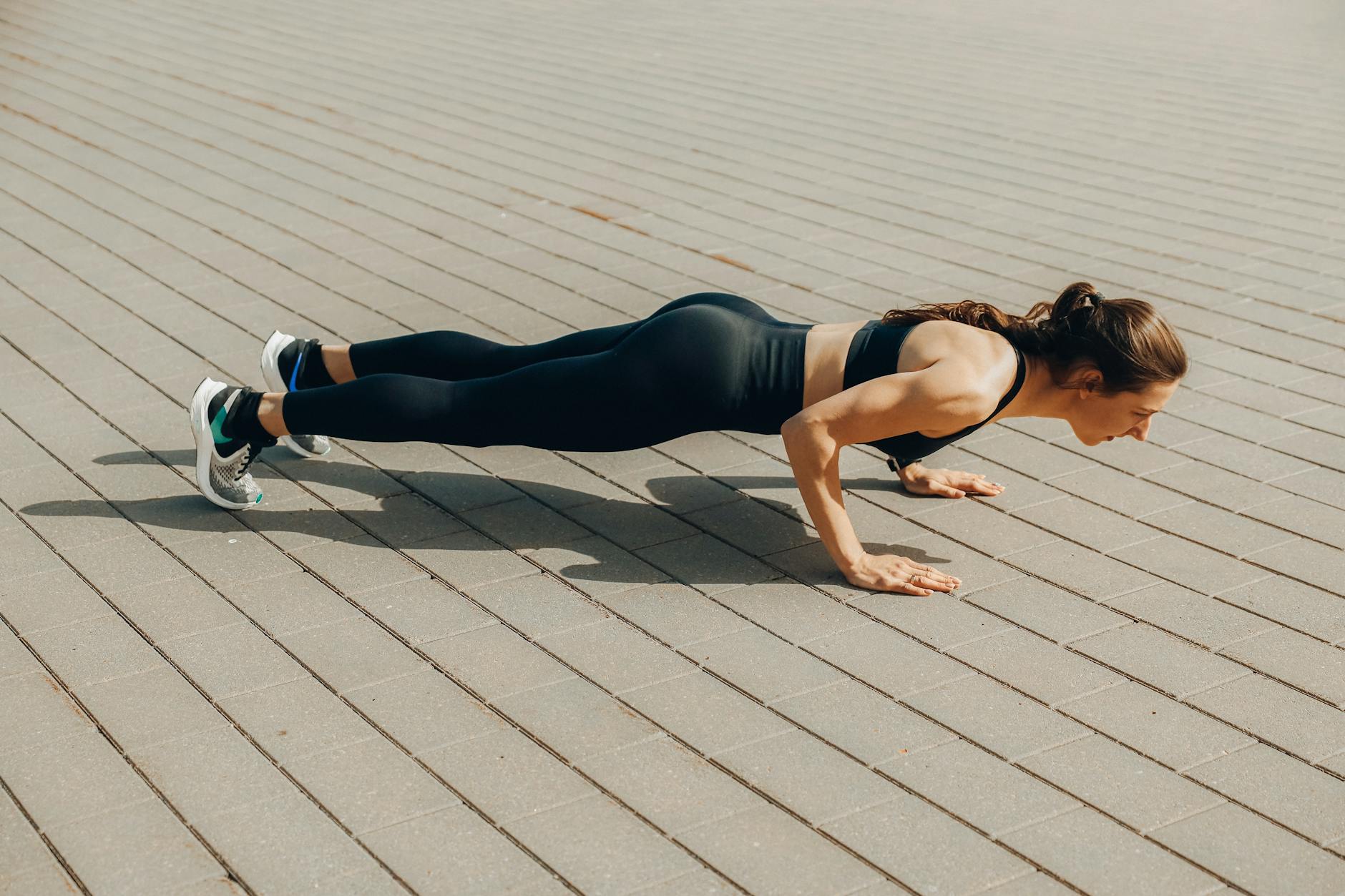Woman performing a push-up exercise outdoors in sportswear, promoting fitness and a healthy lifestyle. - outdoor hiit workouts