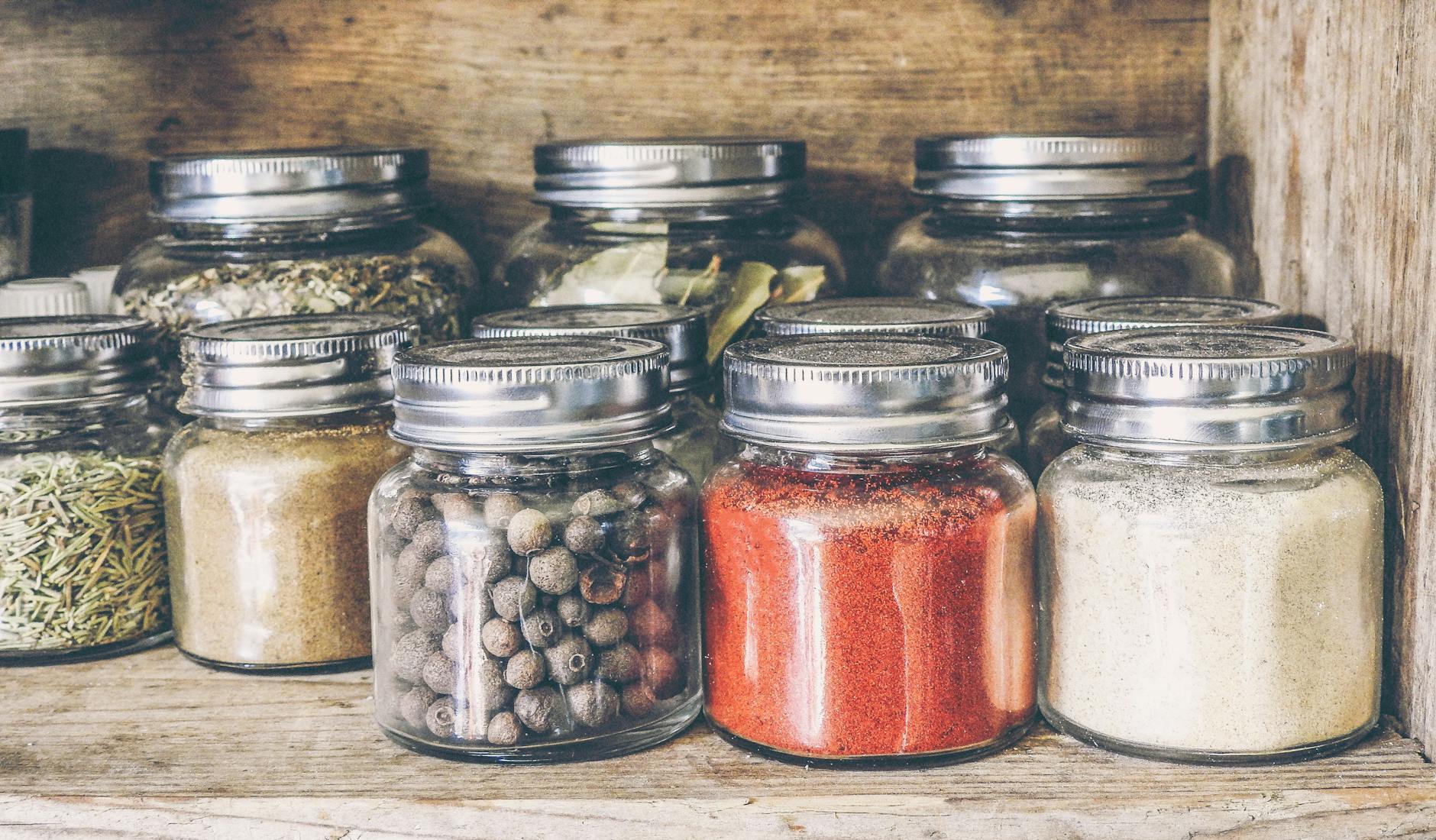 A collection of assorted spices in glass jars on a rustic wooden shelf for culinary use. - pantry cleanout weight loss