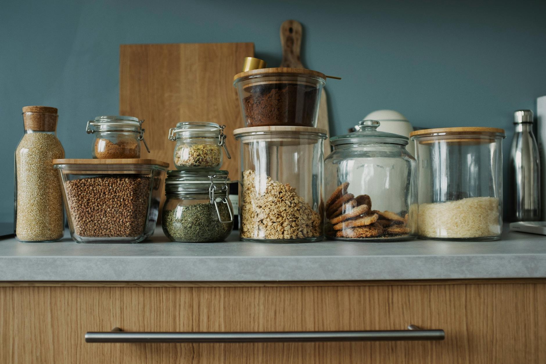 Glass jars with pantry essentials like oats, cookies, and spices on a kitchen counter. - pantry cleanout weight loss