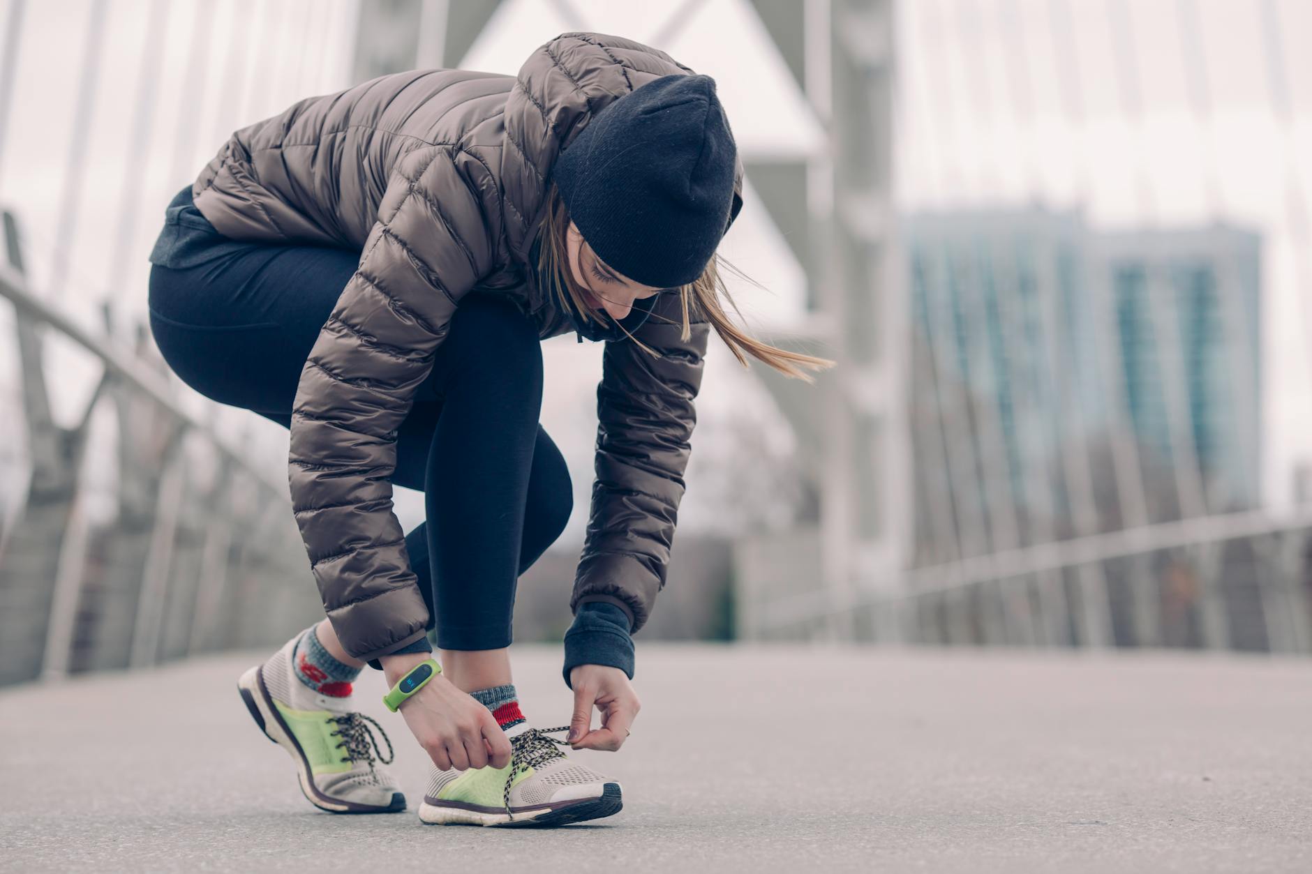 Woman in activewear tying running shoes on a city bridge, ready for a winter jog. - post winter workout