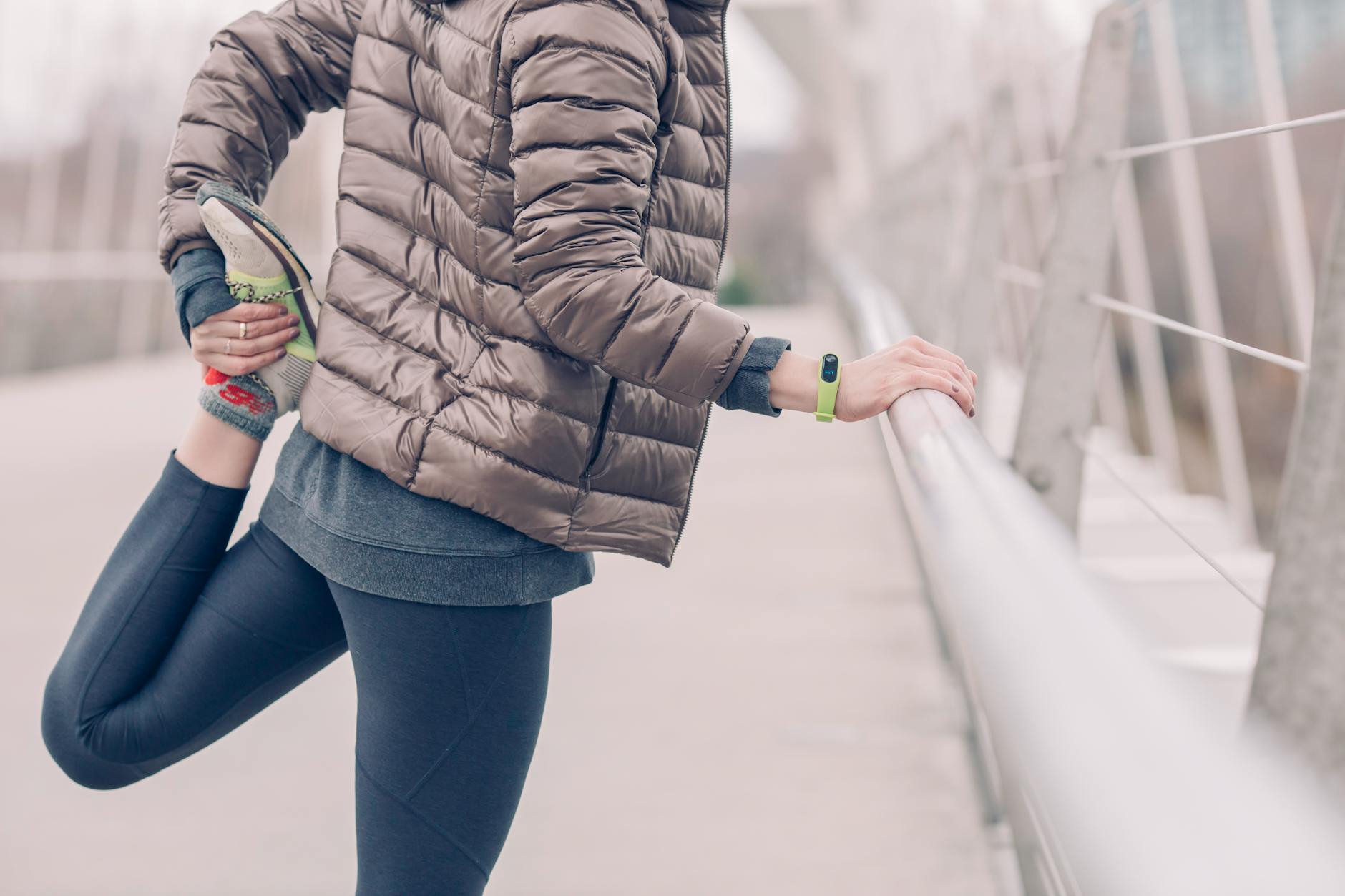 Woman in winter attire stretching outdoors on a bridge, fitness and lifestyle focus. - post winter workouts