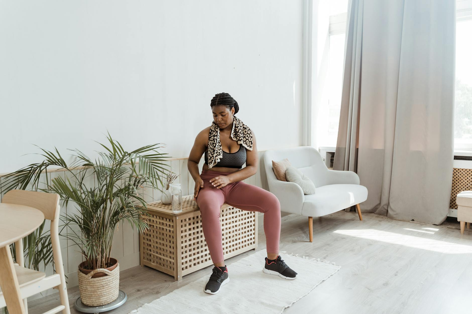 Black woman in activewear resting at home after exercise, sitting on a chair with a towel around her neck. - post winter workouts