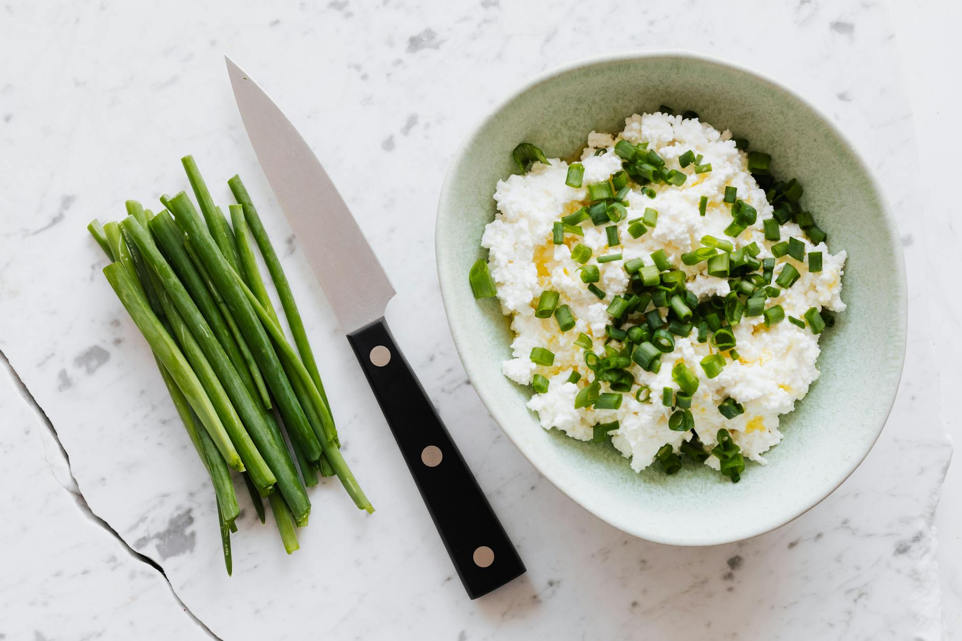 Top view of fresh salad with cottage cheese chopped onion oil and knife fresh greenery on white table with crack - probiotic foods spring