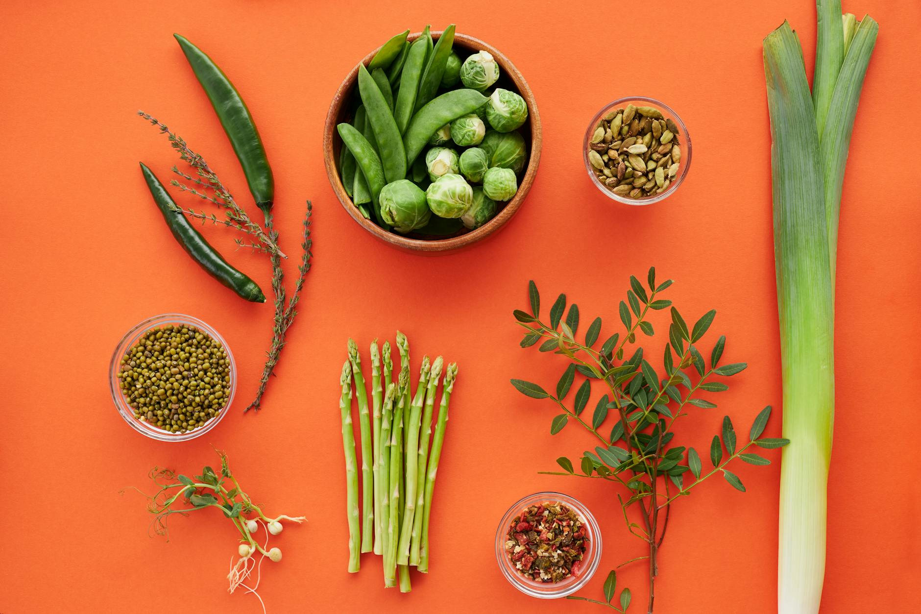 Top view of assorted green vegetables and herbs on a bold orange background, showcasing freshness. - probiotic foods spring