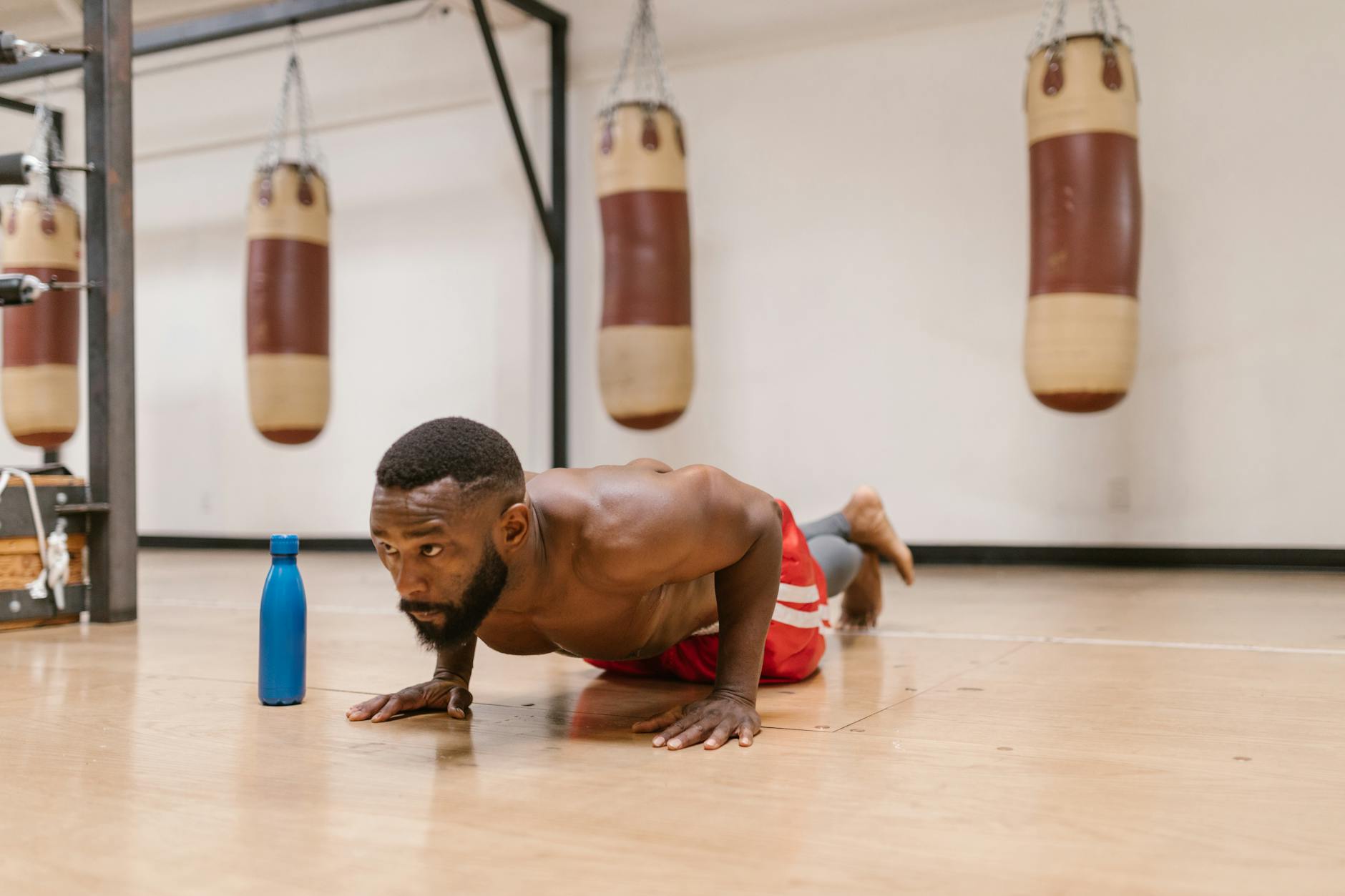 A focused shirtless man performing push-ups on a gym floor beside a blue water bottle. - push day workout