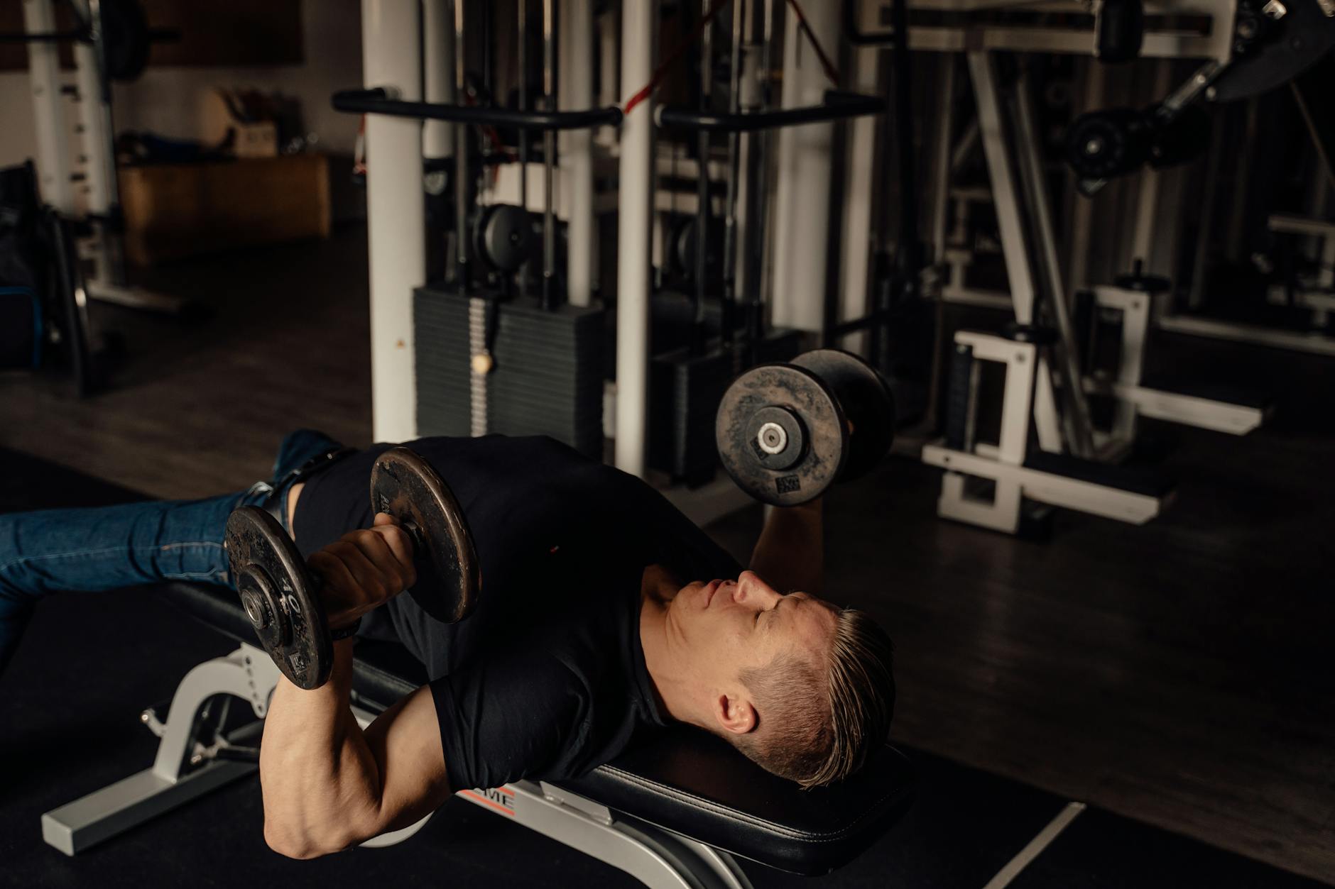 Muscular man doing dumbbell chest press exercise in a gym setting, highlighting fitness and strength. - push day workout