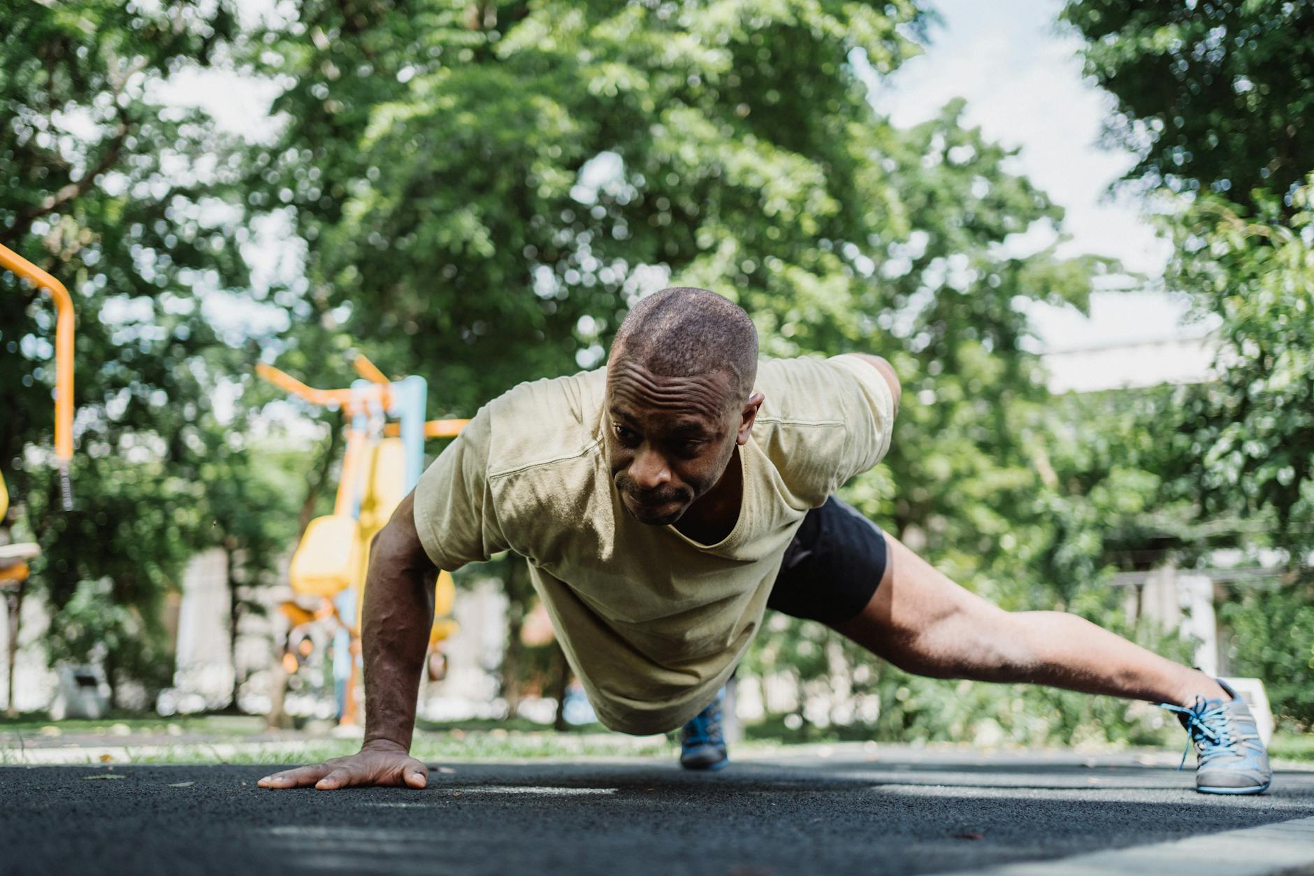 Athletic man performs a one-arm push-up in a lush park setting, showcasing strength and fitness. - push day workout