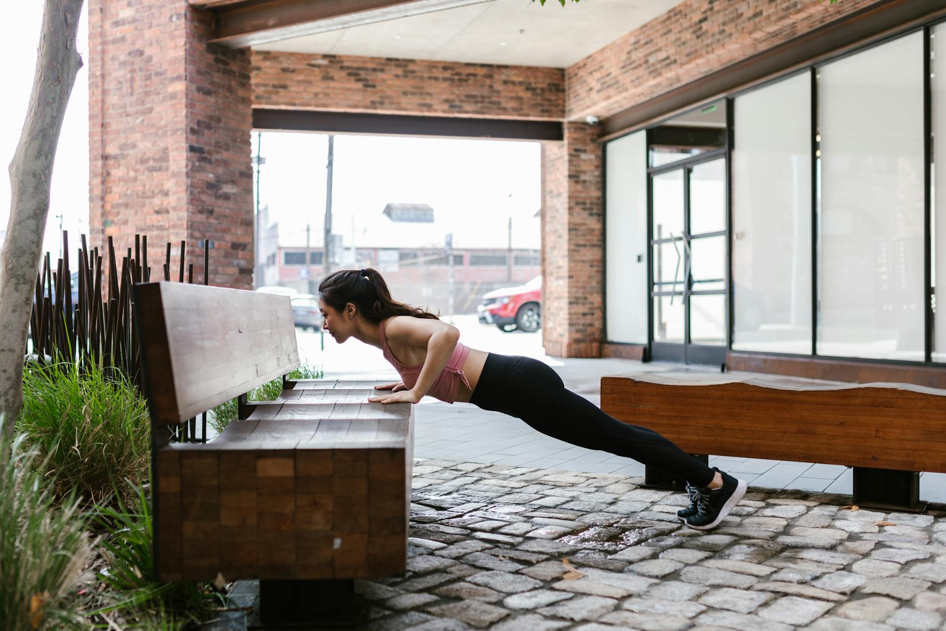 A woman doing a push-up on a bench in an outdoor urban setting, illustrating fitness and healthy living. - push day workout