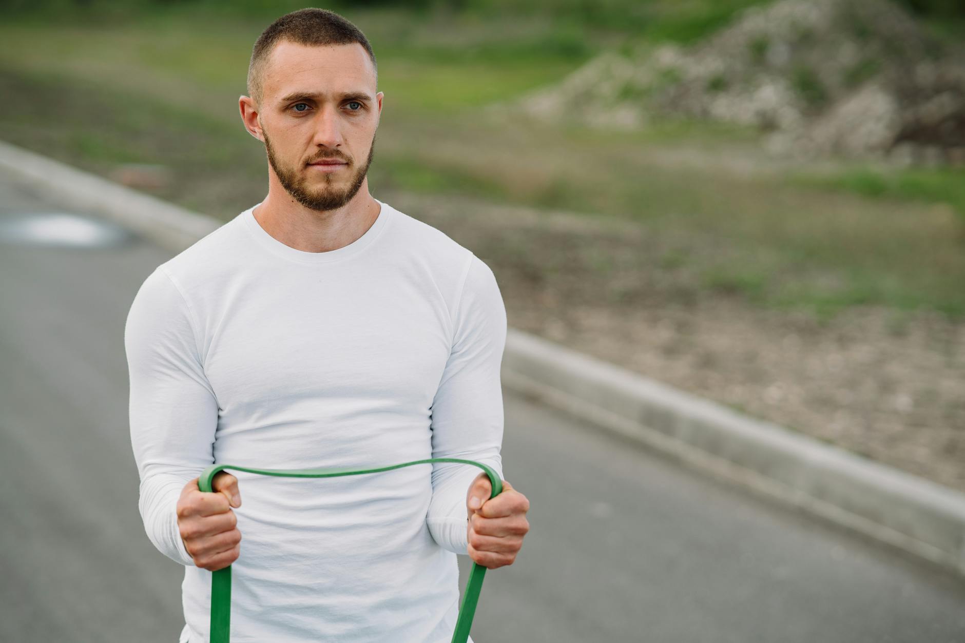 Adult man working out with a resistance band on an outdoor road. - resistance training benefits