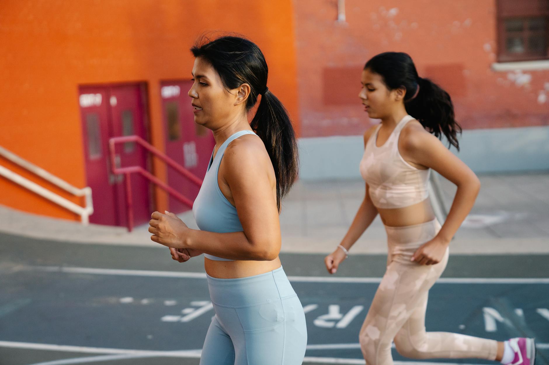 Two women in athletic gear jogging on a city pavement, promoting health and fitness. - running plan for beginners