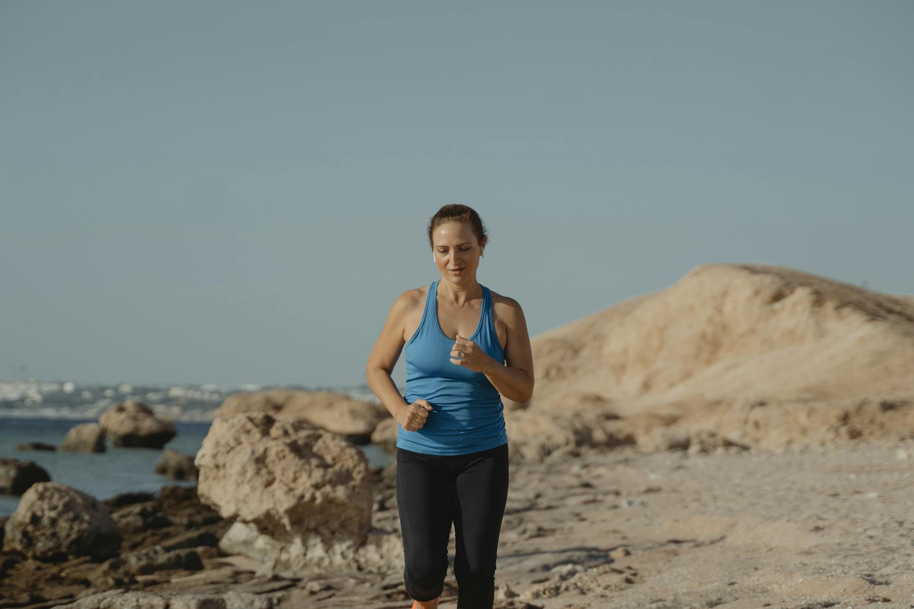 Woman jogging on a rocky beach path, promoting fitness and healthy lifestyle. - seasonal blues exercise