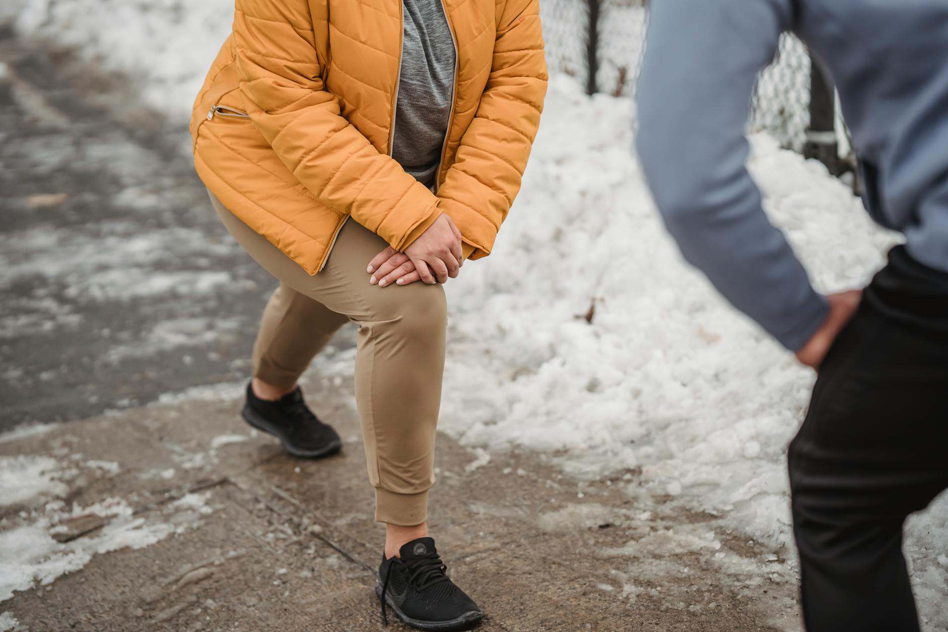 Unrecognizable plump woman in warm outerwear doing stretching exercise with anonymous personal trainer while training in winter park with snow - seasonal blues exercise