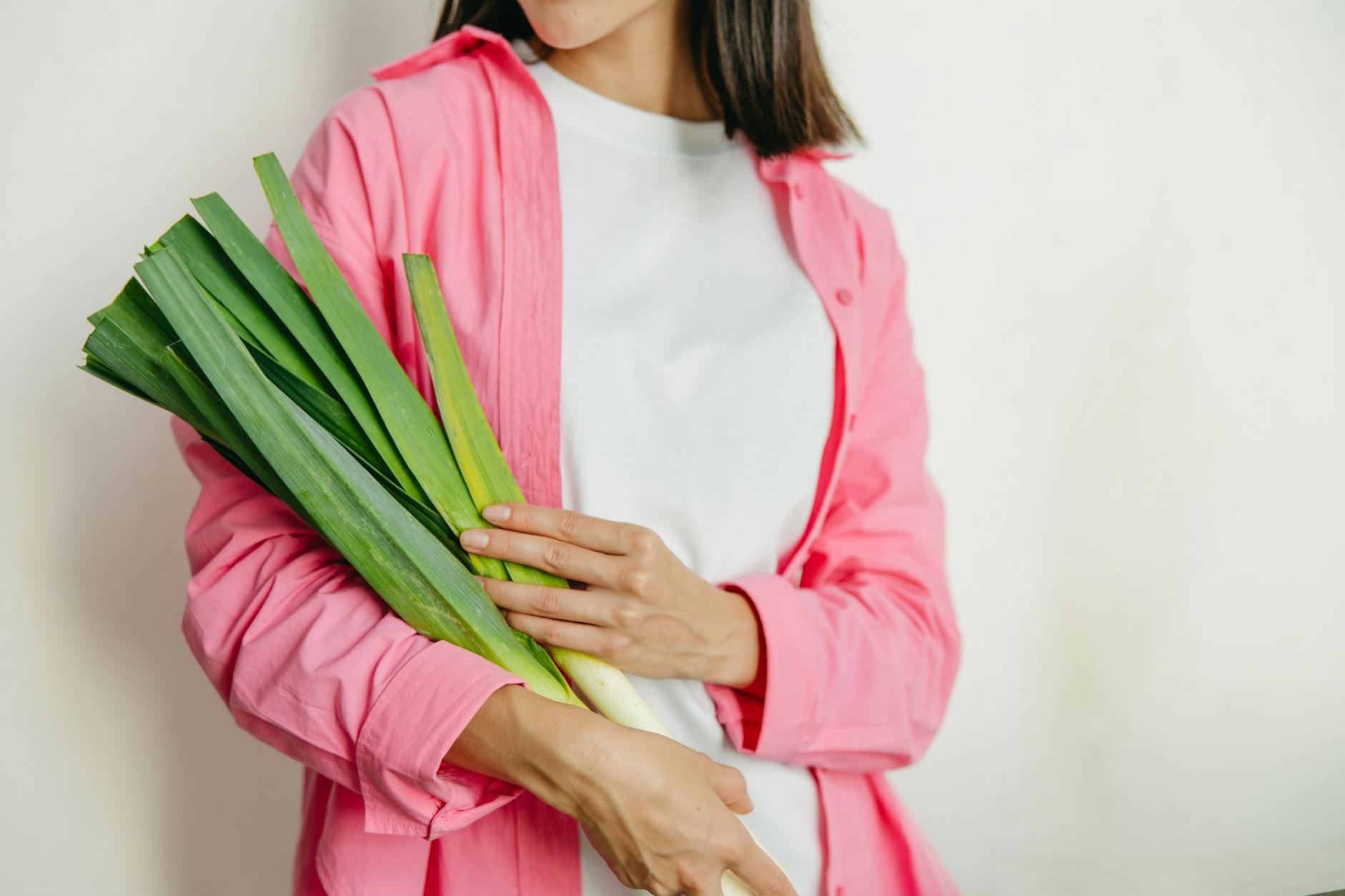 A woman in a pink jacket holding fresh spring onions against a white background. - seasonal produce spring
