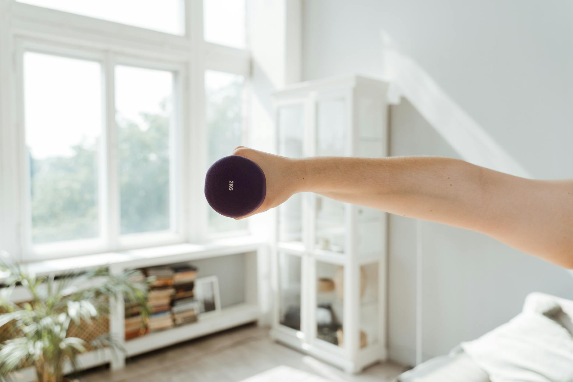 Close-up of a person lifting a 2kg dumbbell in a sunlit room. - small space workouts