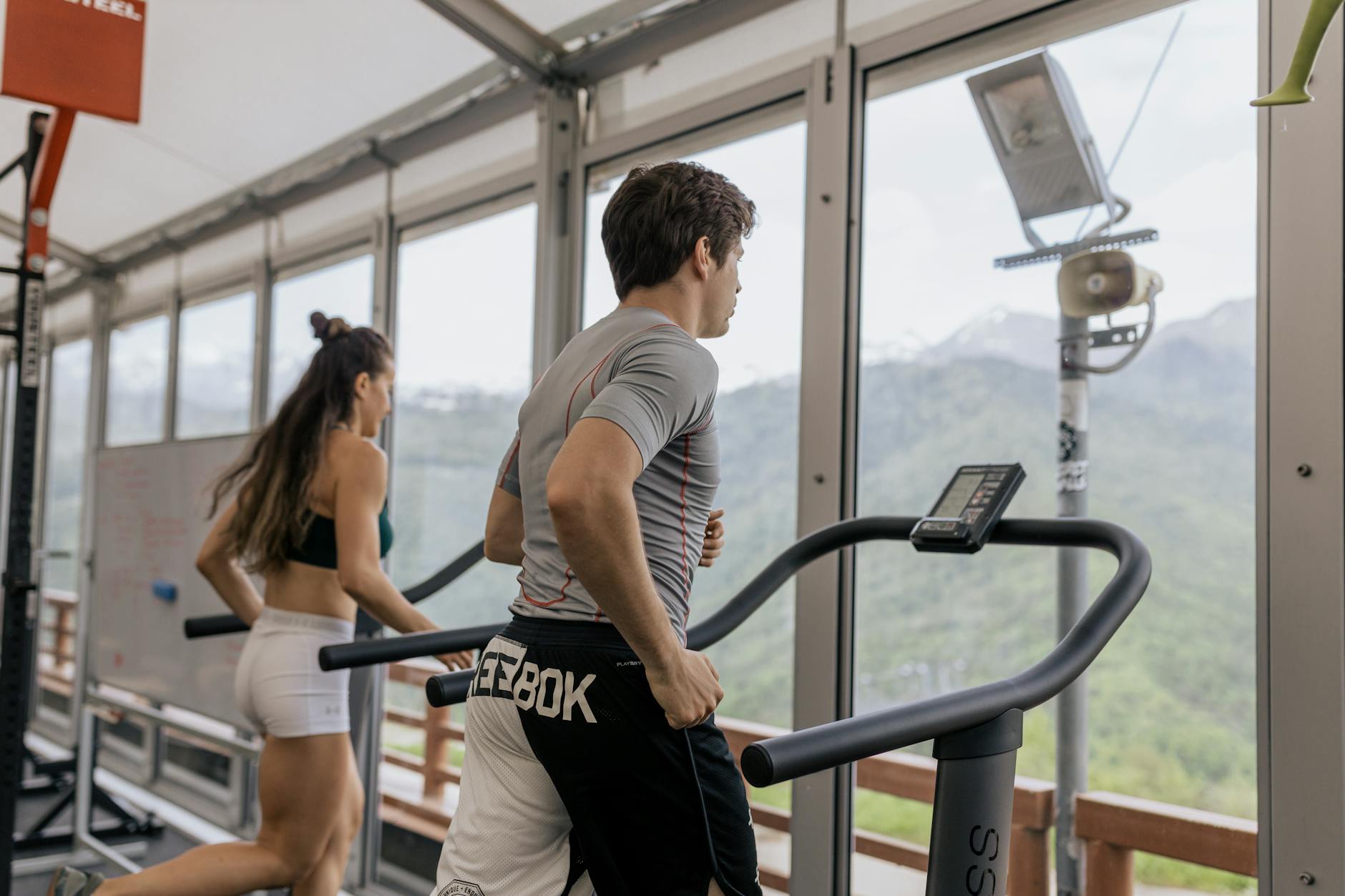 Two people running on treadmills in a gym with a mountain view, promoting fitness. - spring cardio fat burn