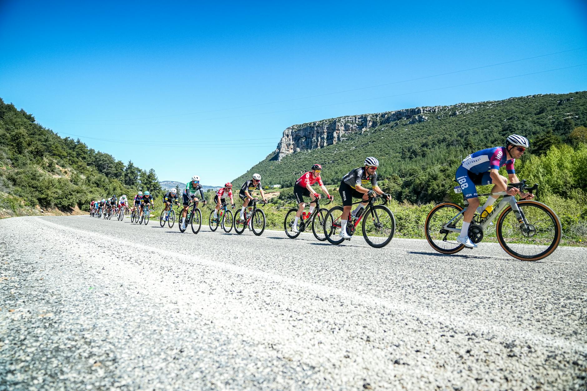 Professional cyclists speed through mountainous terrain in Mersin, Türkiye on a sunny day. - spring cycling routes