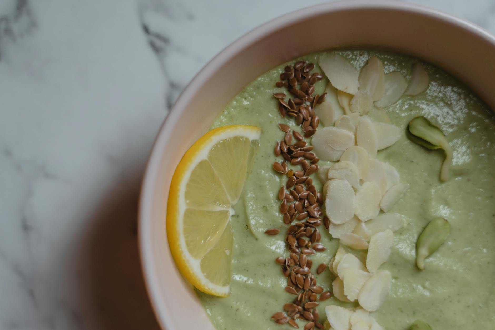 Healthy green smoothie bowl topped with almonds, flax seeds, and lemon slice for a nutritious meal. - spring energy smoothie