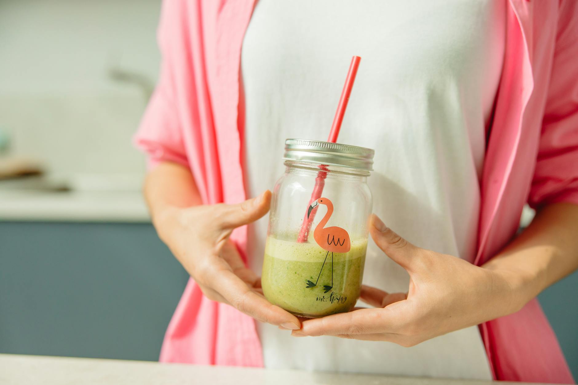 Close-up of a woman holding a green smoothie in a glass jar, promoting healthy living. - spring energy smoothie