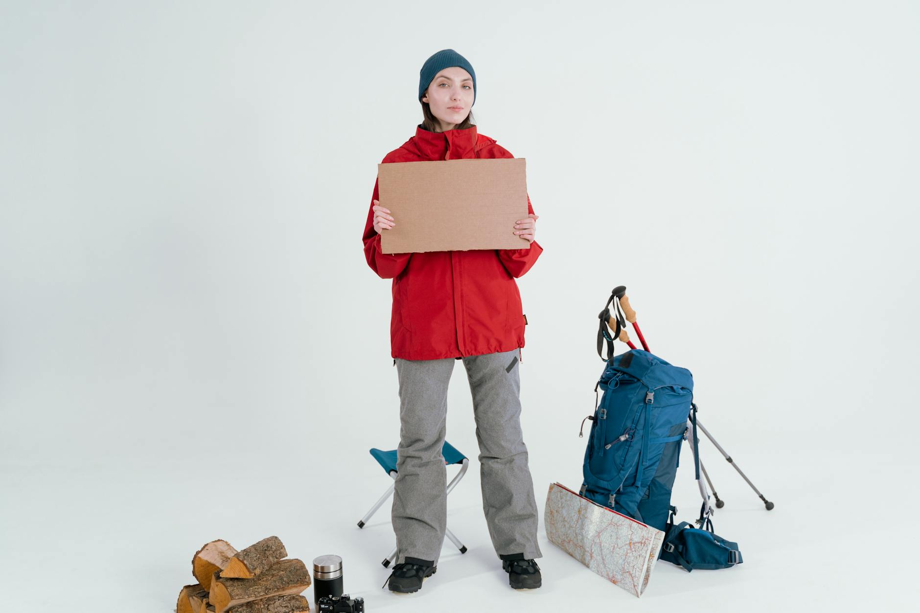 Woman in winter gear holding a blank cardboard with camping items, ready for adventure. - spring hiking gear