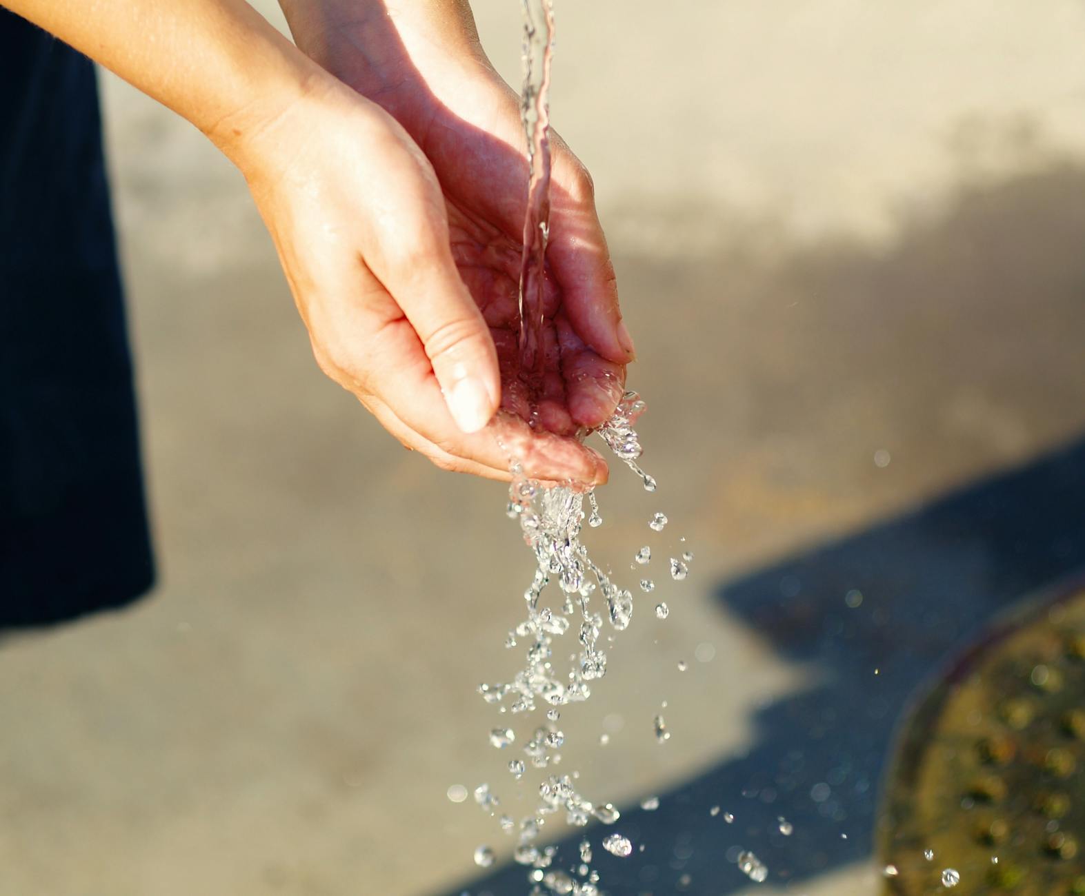 Close-up of hands catching flowing water outdoors, symbolizing freshness and purity. - spring hydration plan