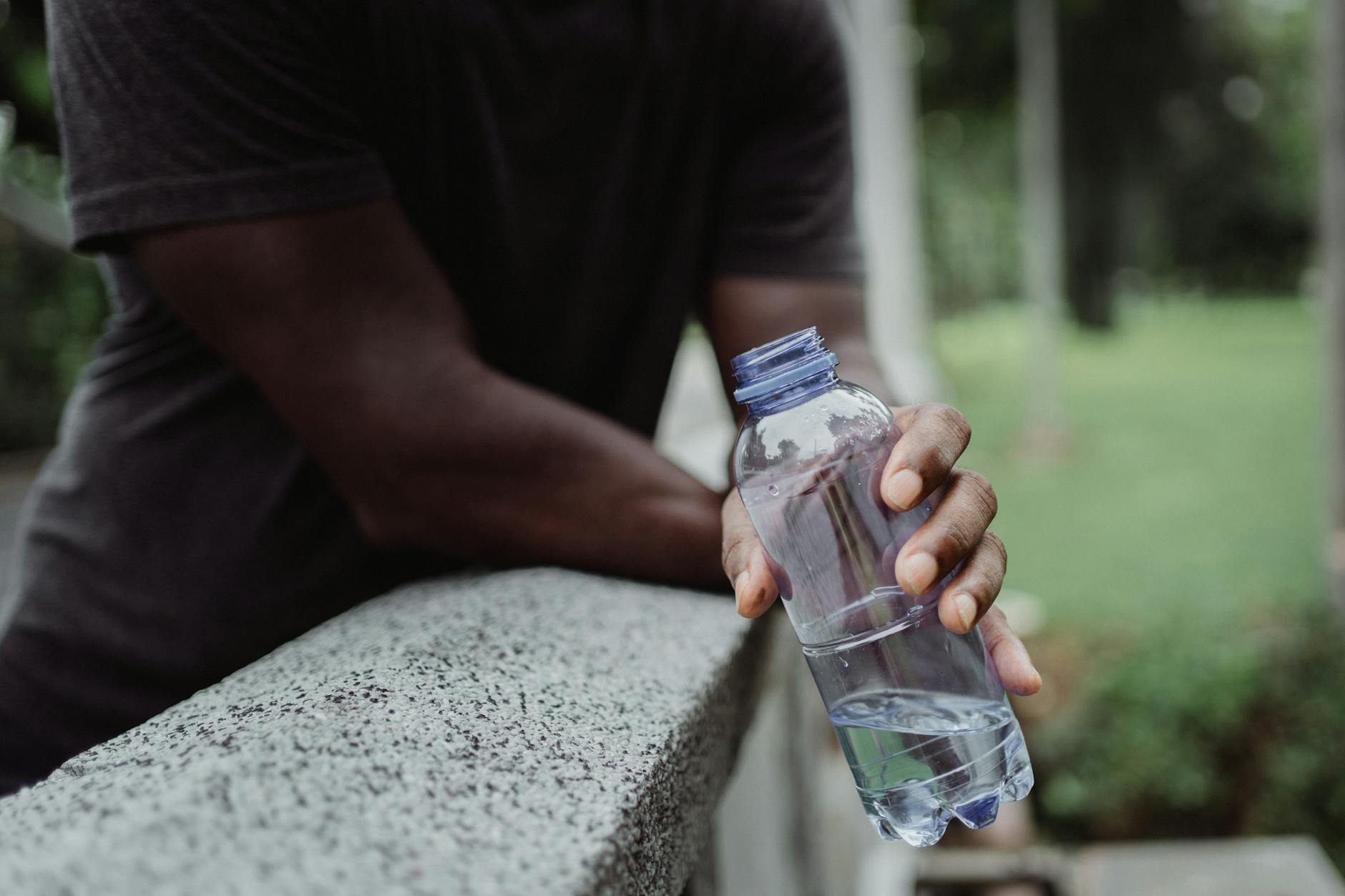 A person holds a plastic water bottle on a concrete rail outdoors, emphasizing hydration. - spring hydration plan