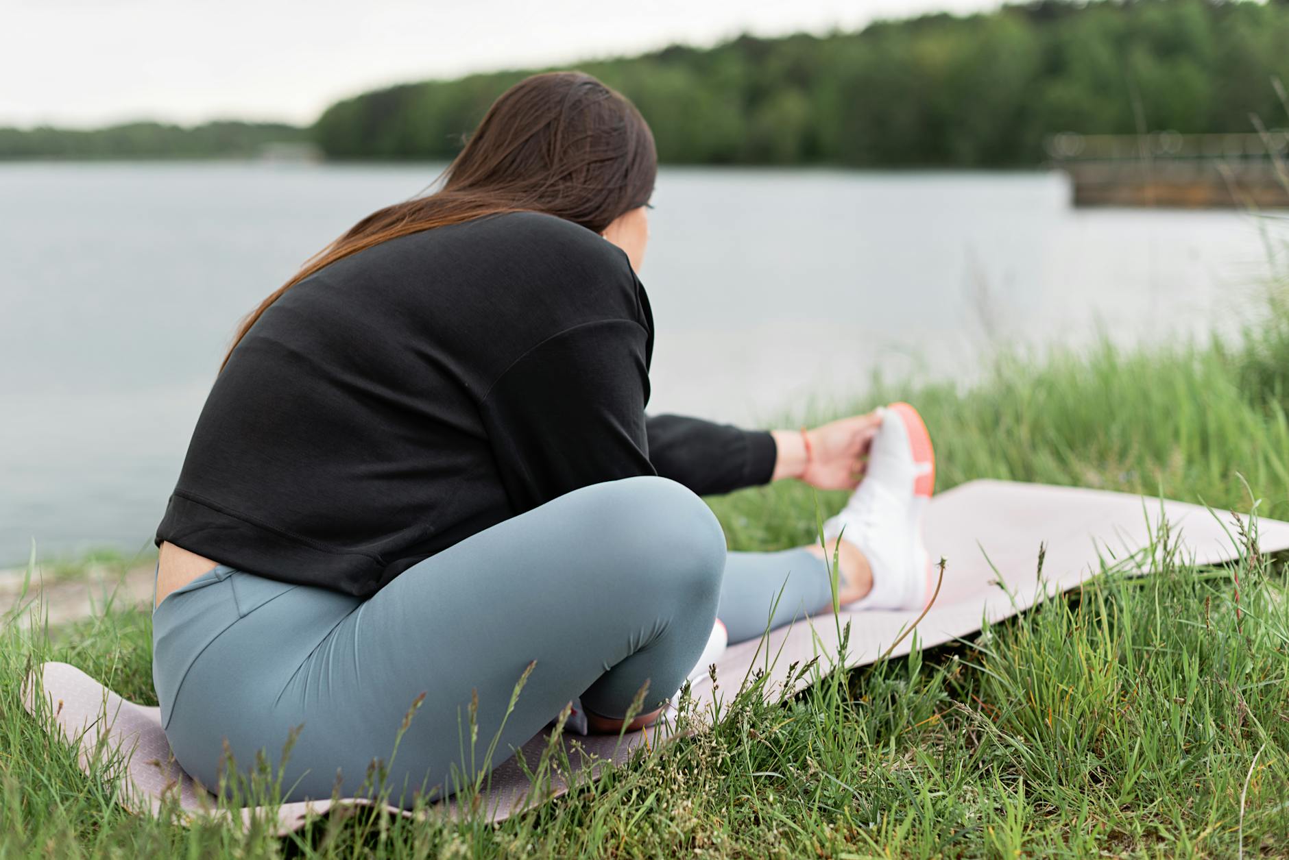 Woman doing stretching exercises on a yoga mat outdoors by a serene lake. - spring outdoor exercise mental health