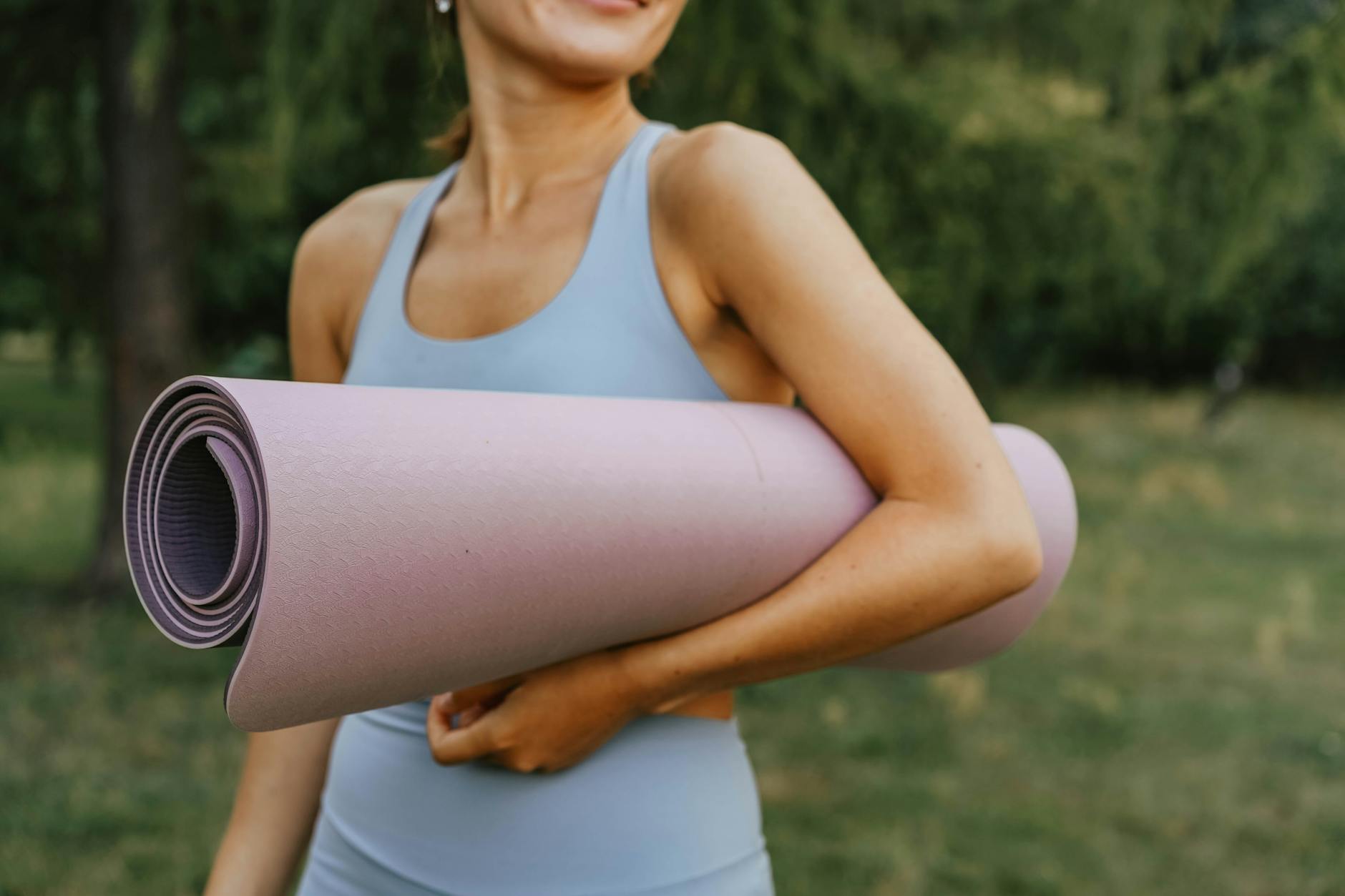 An active woman in sportswear holding a yoga mat outdoors, ready for fitness. - spring outdoor workouts